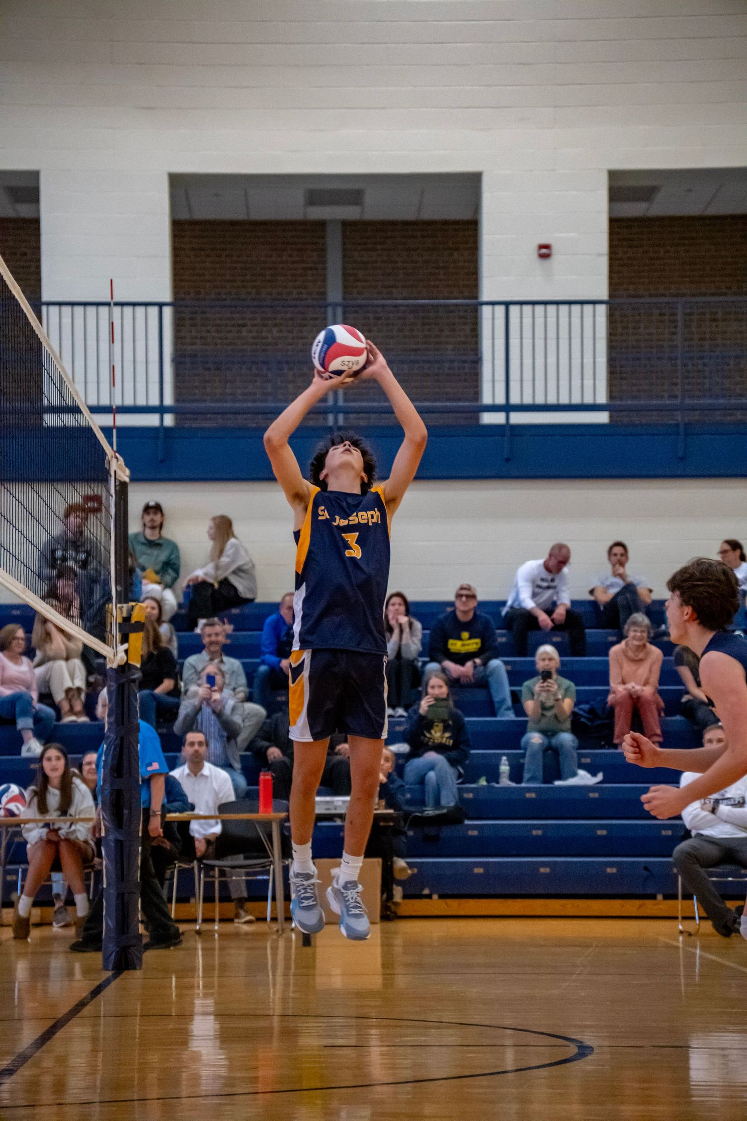 Player in navy uniform sets volleyball during competitive indoor match.