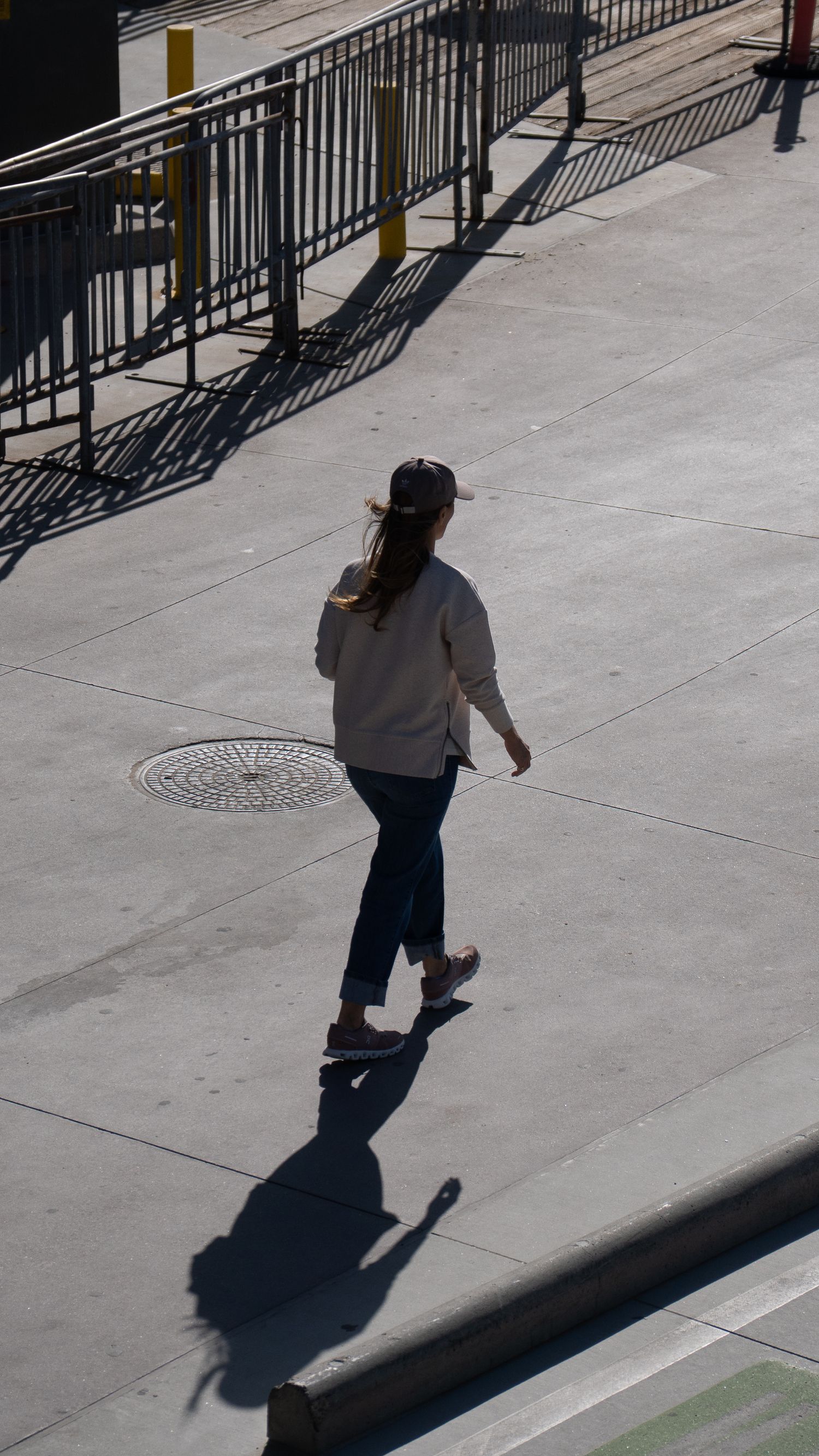 A person walking casts a long shadow on concrete sidewalk next to metal railings.