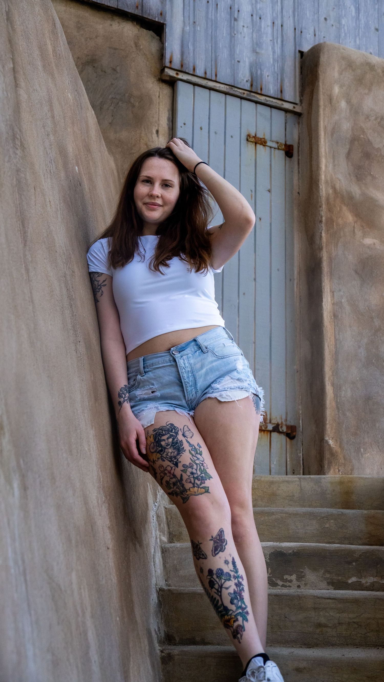 Person in casual summer outfit posing on concrete steps with artistic tattoos visible.