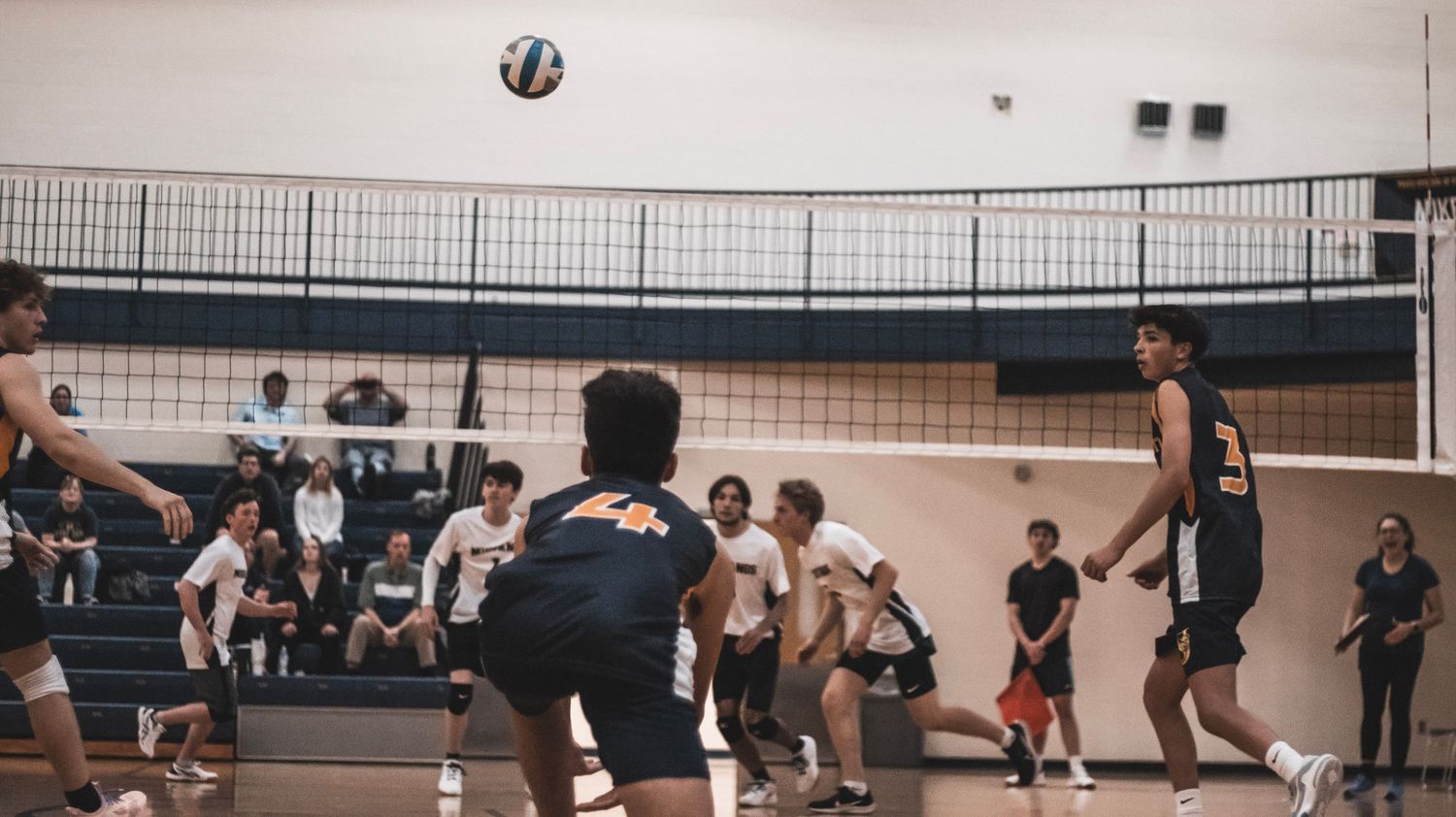 Indoor volleyball game in progress with teams competing on opposite sides of net.