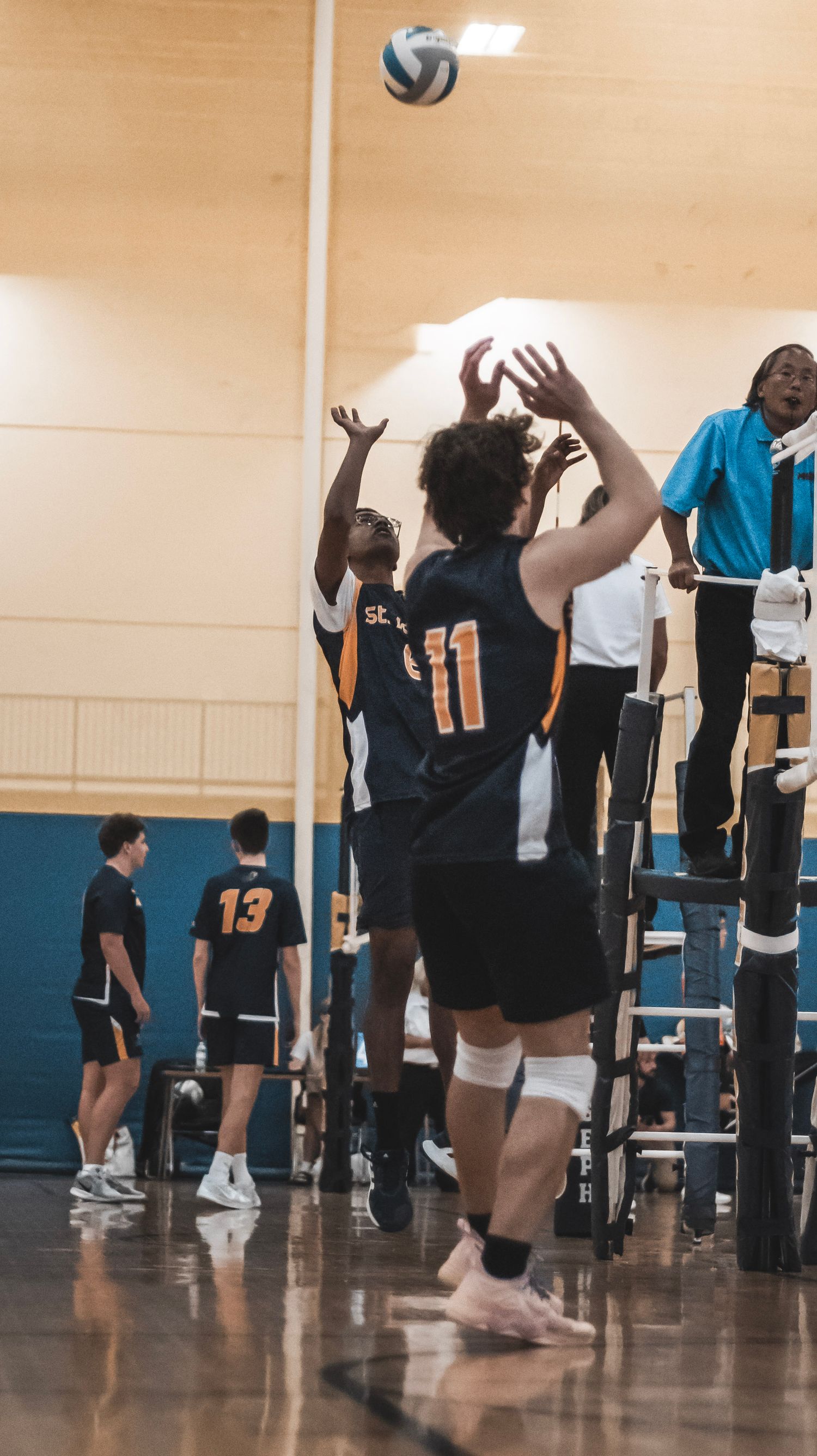 Players jump at the net to block a volleyball during an indoor game.