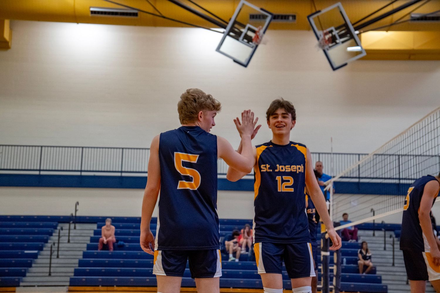 Two teammates in navy uniforms giving each other a high five during a volleyball game.