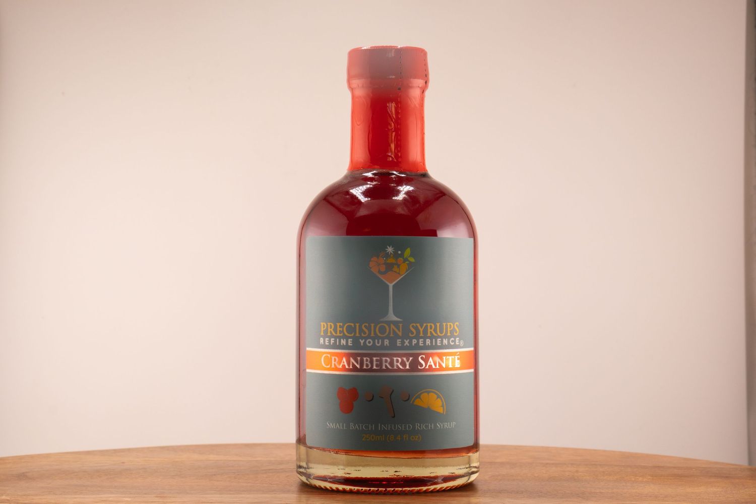 Red-capped spirits bottle with gray label featuring tree logo on wooden surface.