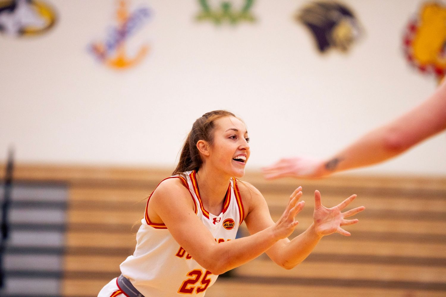 Smiling female basketball player in a white and orange number 25 Bulldogs jersey reaches out to catch a pass during a game.