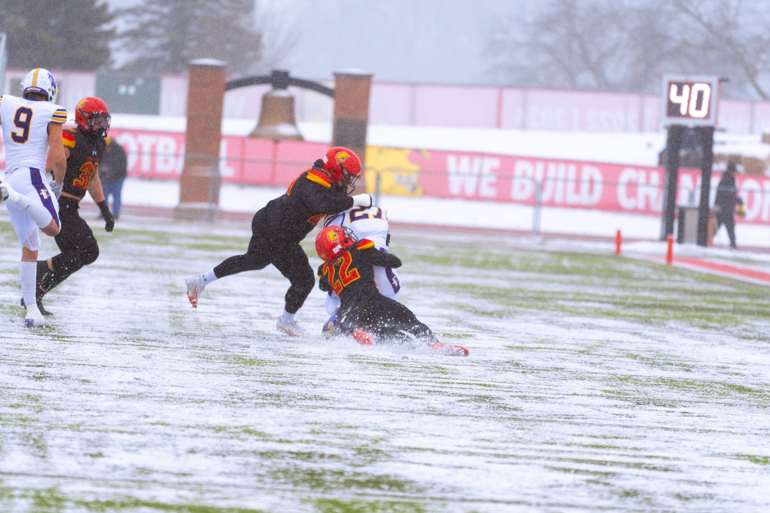 Football players slide and tackle in snowy conditions during an intense winter game on a snow-covered field.