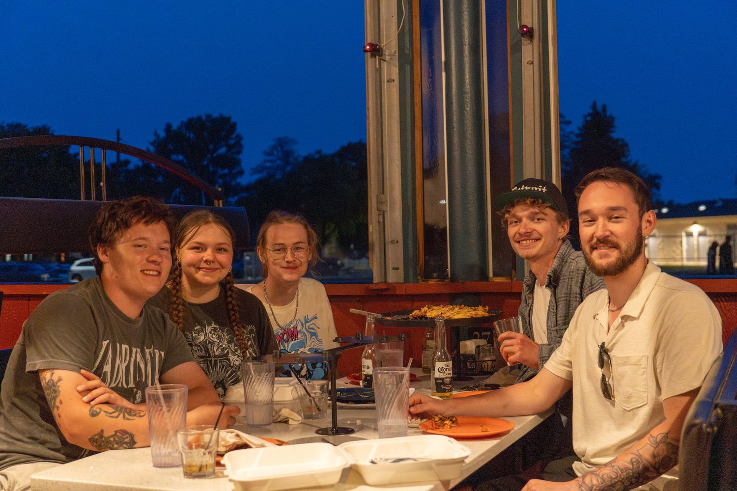 People gathered around a table for a social gathering at twilight with a blue sky visible through windows.