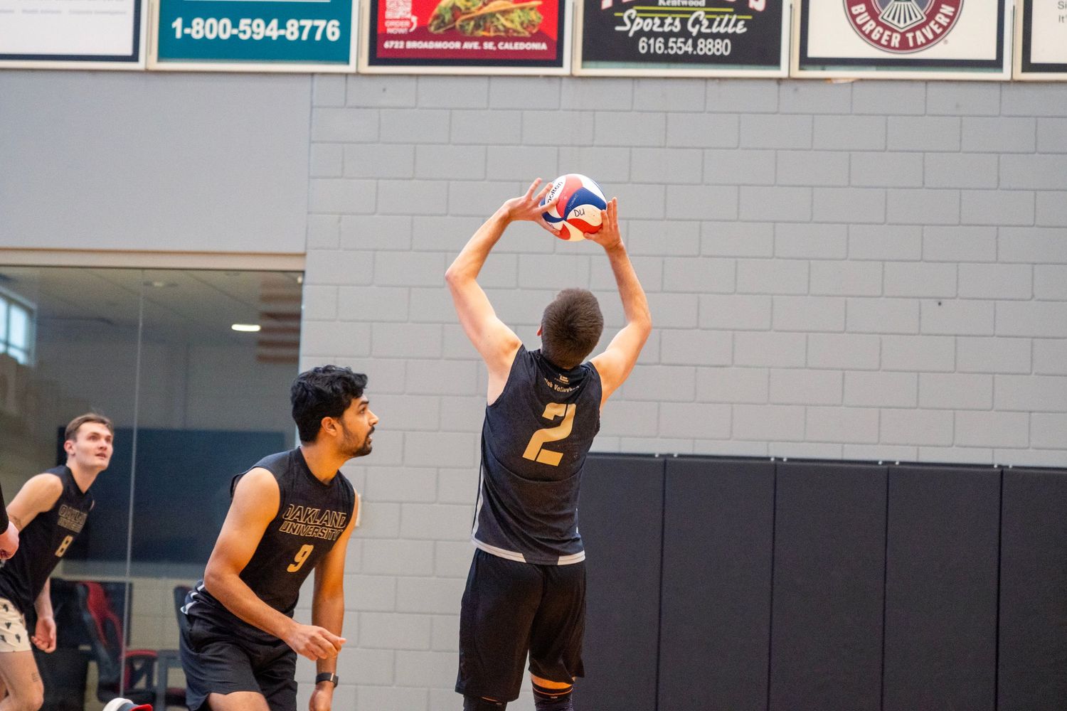Players in black jerseys jumping to block during a competitive volleyball game.
