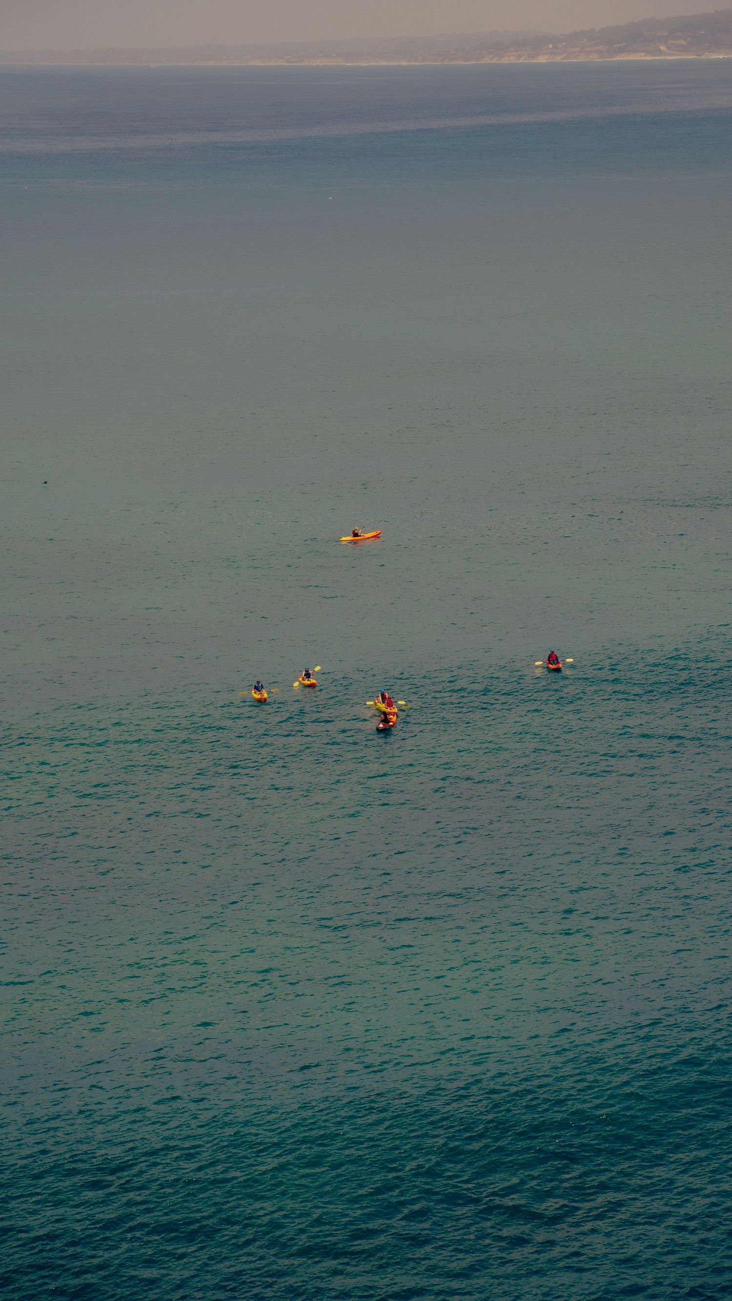 Aerial view of kayakers floating in calm blue-green ocean waters.