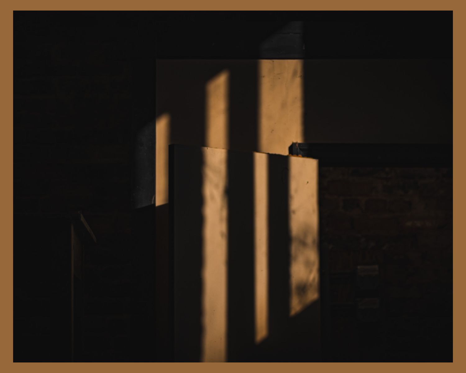 Dramatic shadows cast by sunlight through window panes creating geometric patterns on wall.