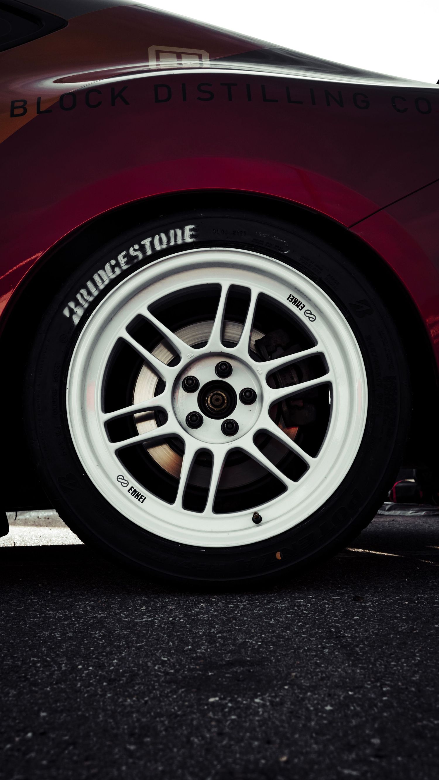 Close-up of a white Bridgestone racing wheel on a burgundy vehicle.