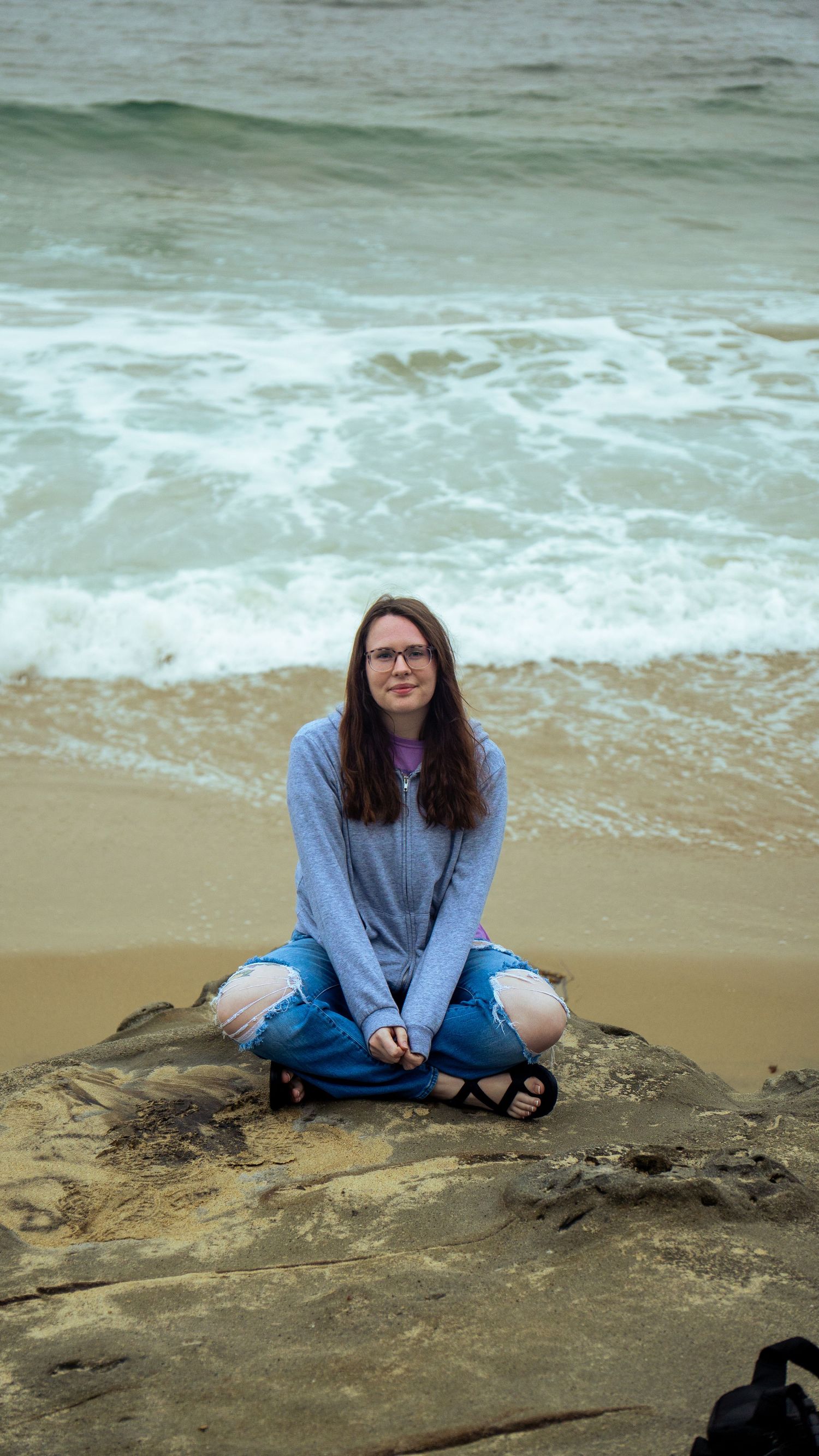 A casual beach portrait on rocky outcrop with waves washing up in the background.