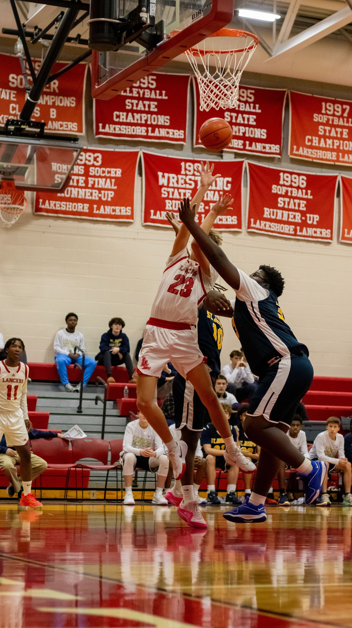 Basketball players competing for rebound during game under championship banners.
