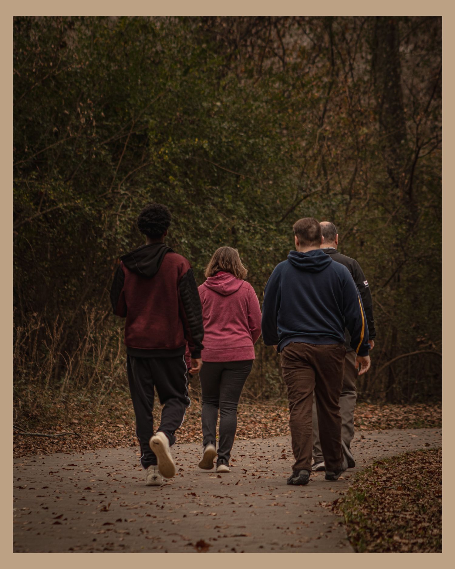 Three people walking together on an autumn trail through woods.