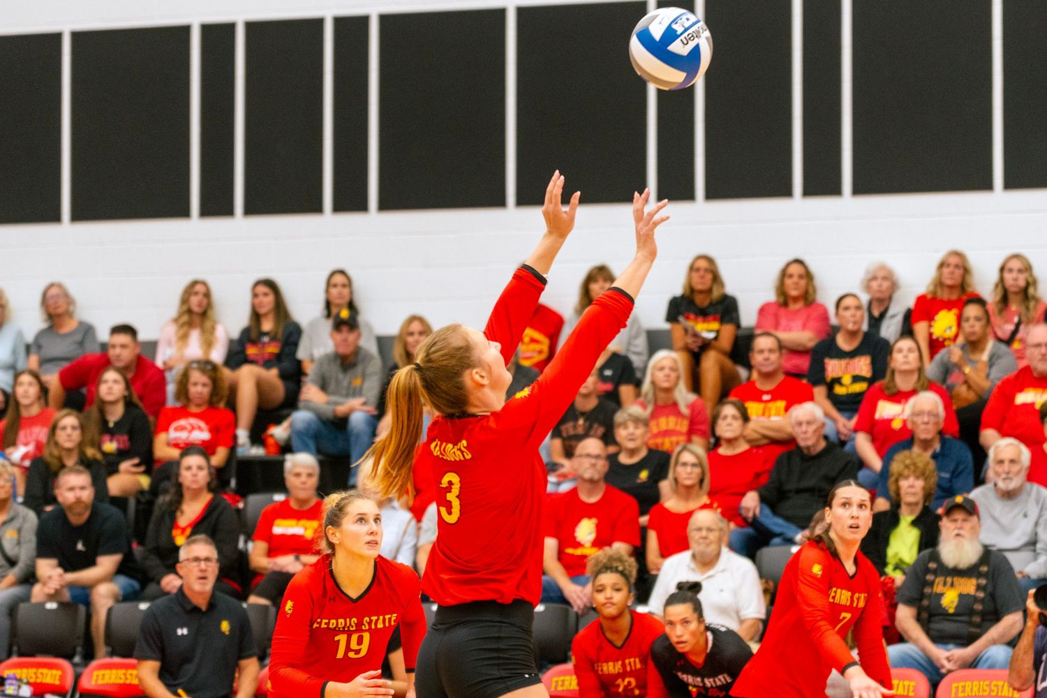 Volleyball players in red uniforms celebrate during an intense match as spectators watch from the stands.