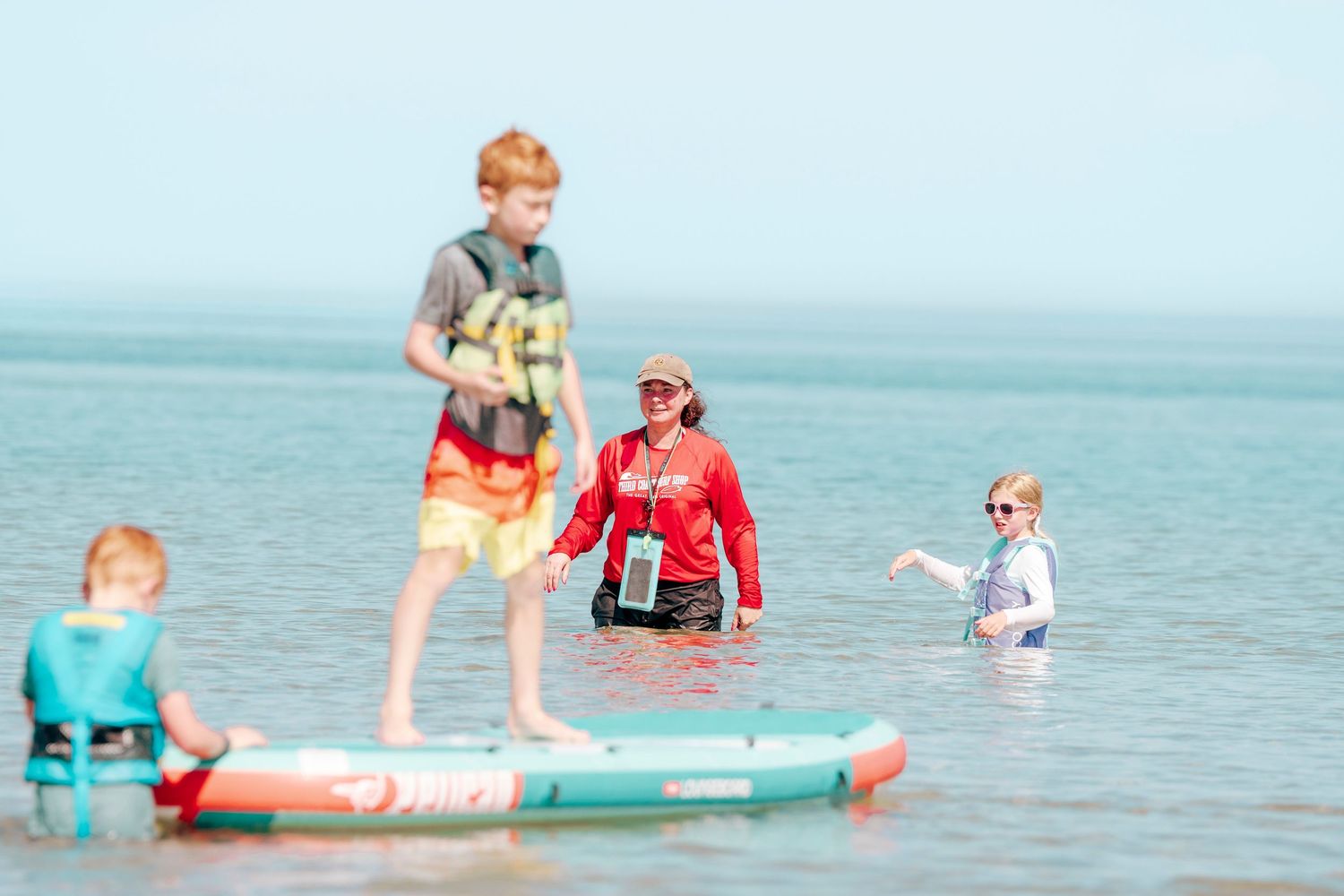 People enjoying a sunny day at the beach with paddleboards and swimming in turquoise blue waters.
