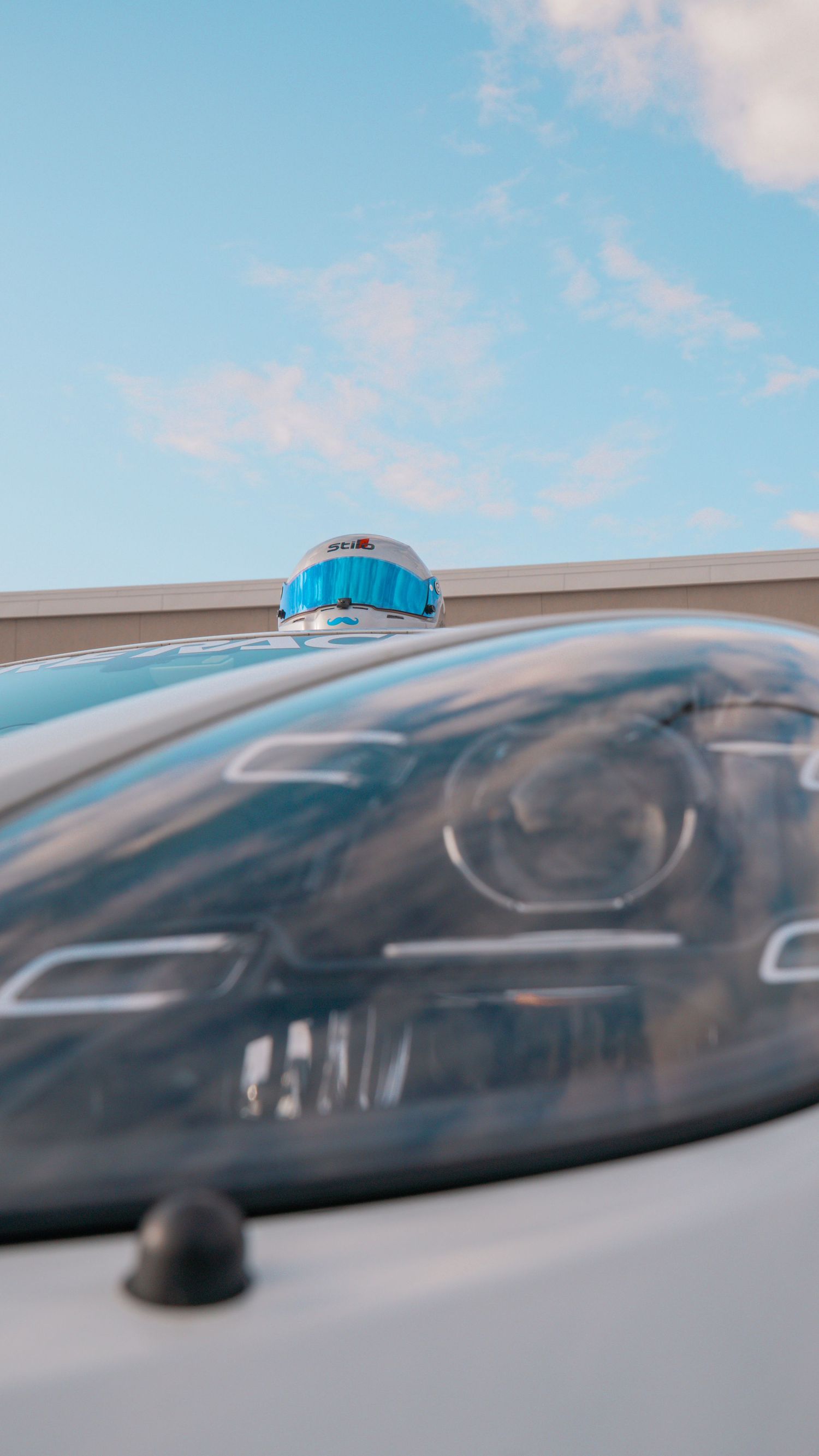 Low angle close-up shot of a sleek black sports car against a bright blue sky with wispy clouds.