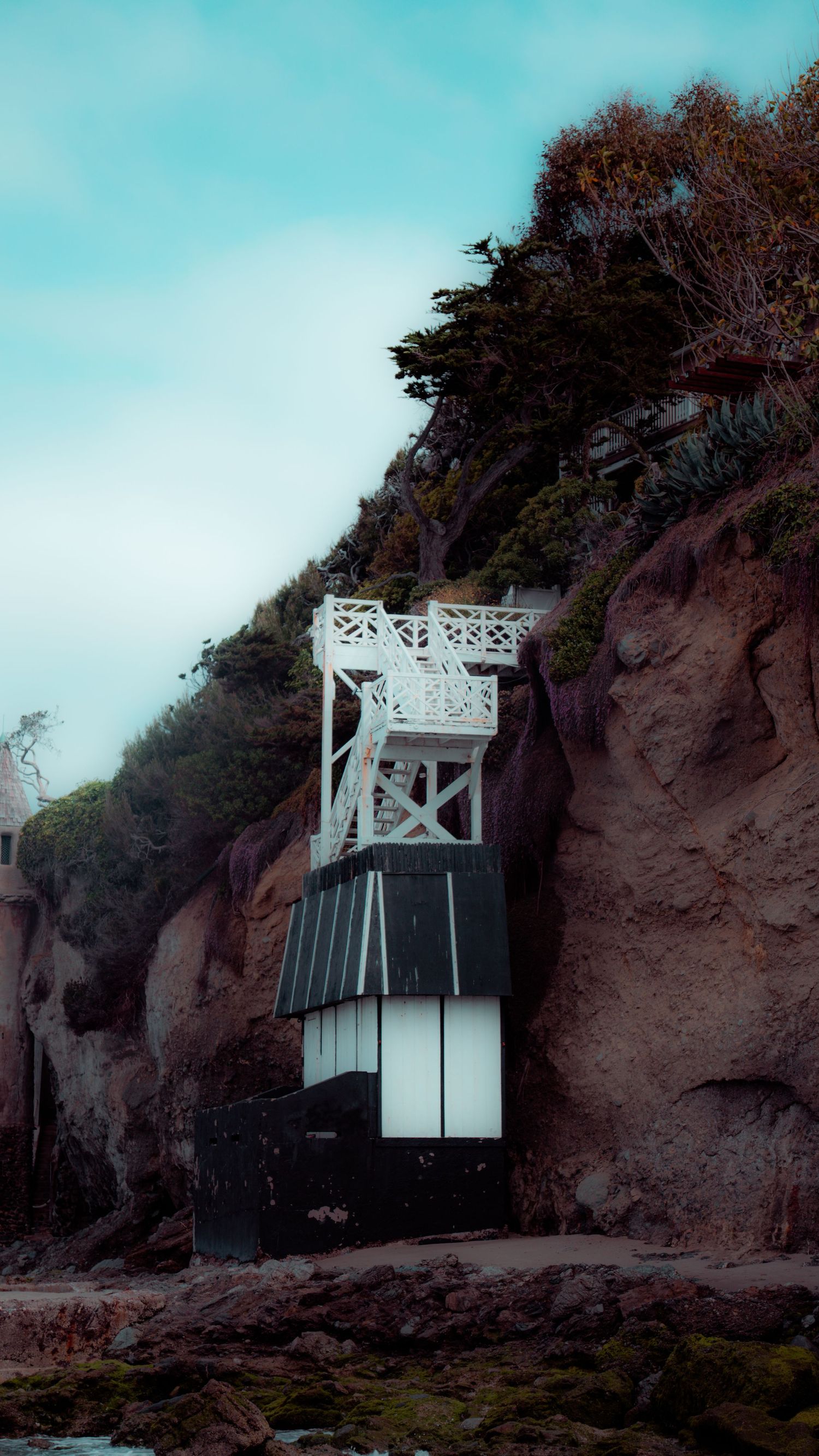 White lighthouse structure built into rocky coastal cliff face against turquoise sky.