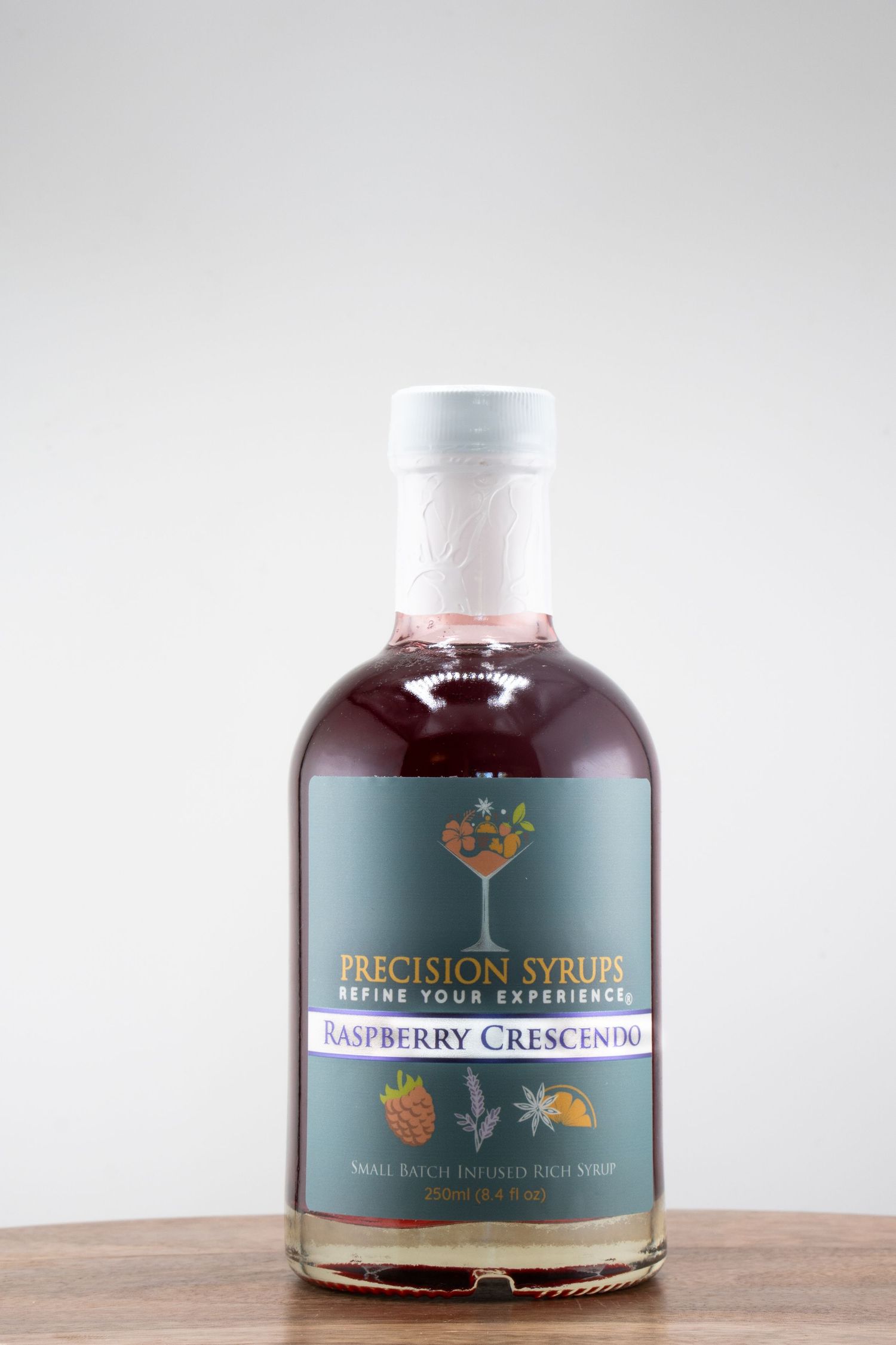 A bottle of Raspberry Crescendo Precision Syrup with a white cap on a wooden table.