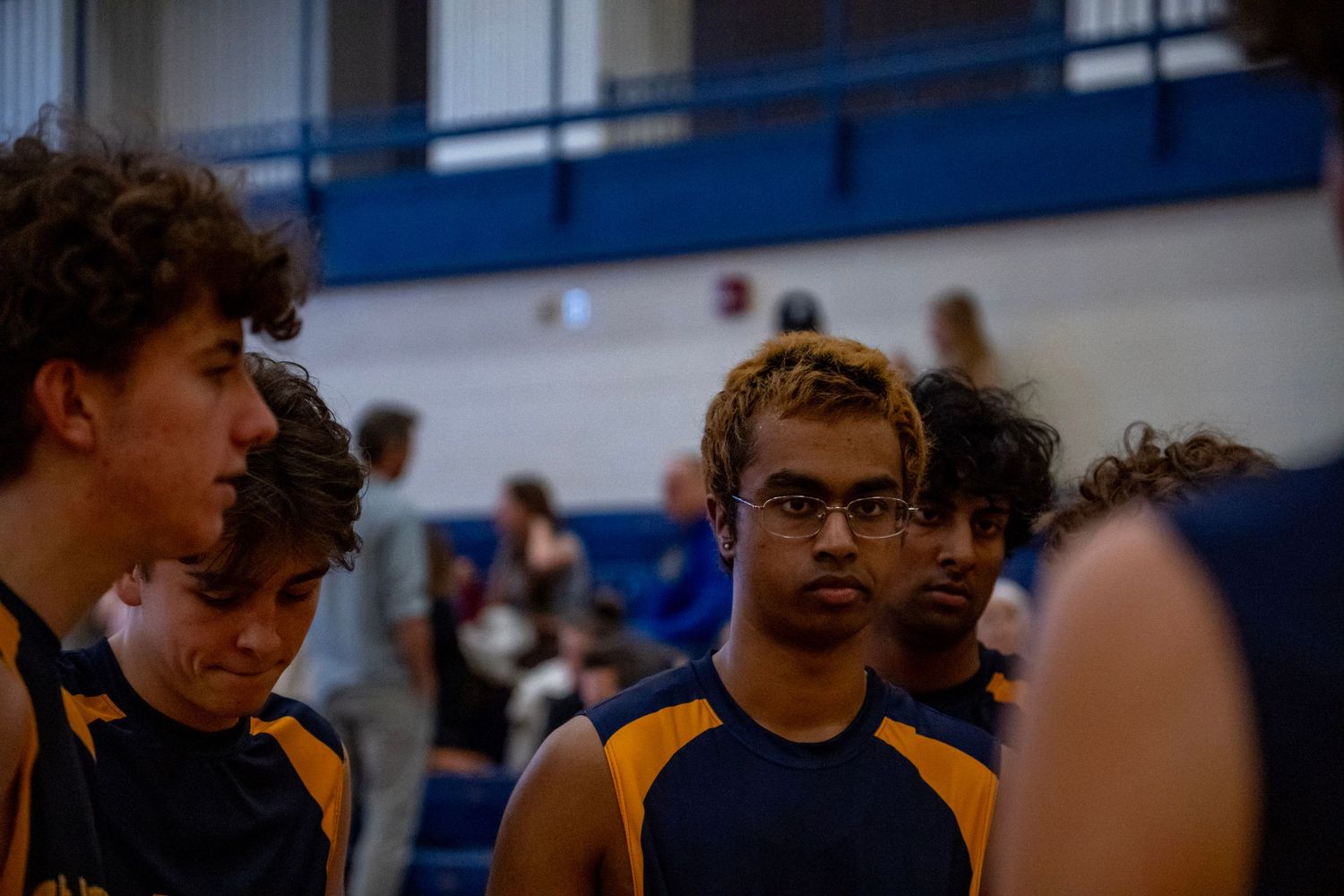 Players in navy and gold uniforms huddle during a volleyball game.