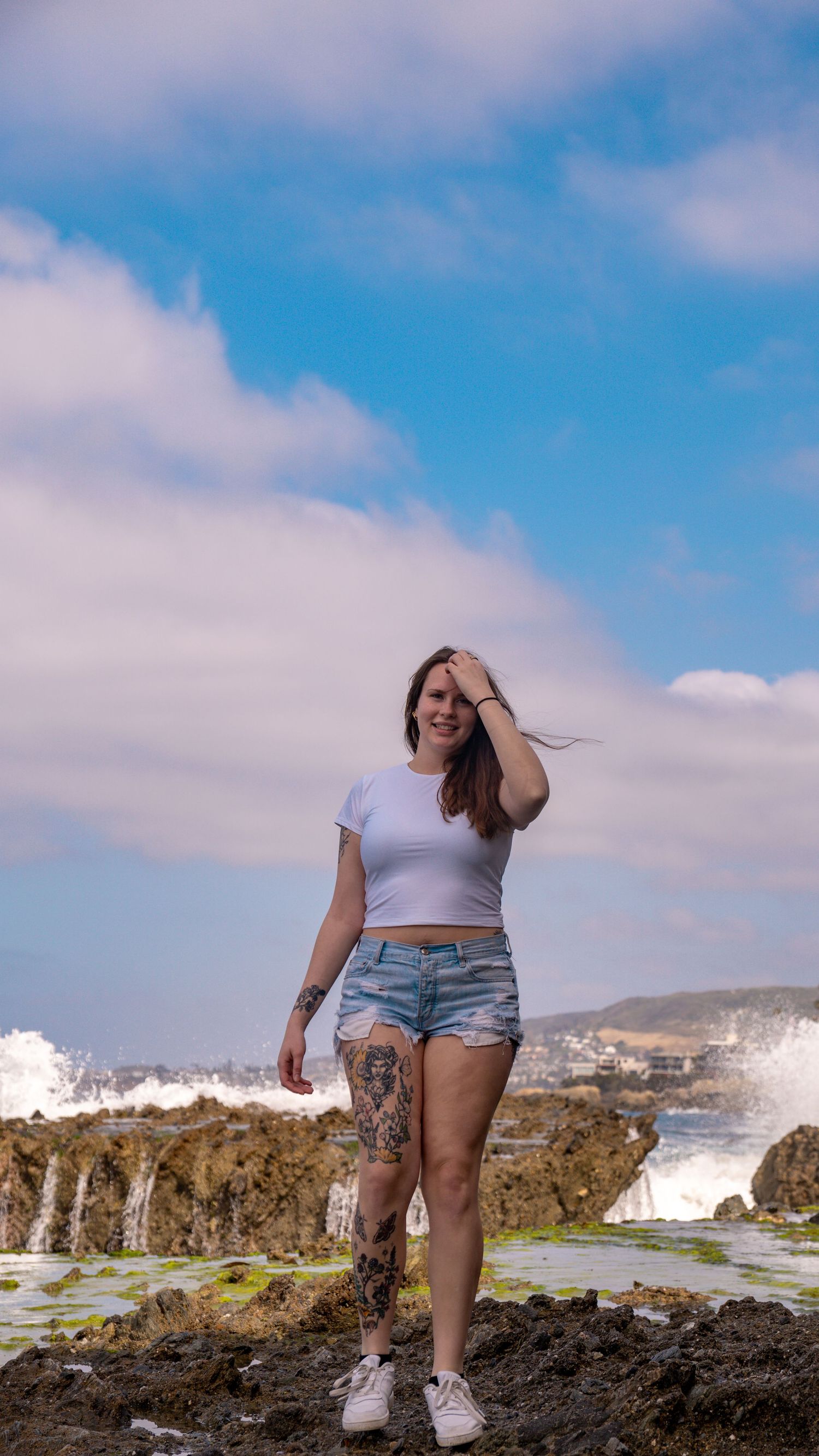 Person enjoying scenic coastal views on rocky cliff with ocean spray visible.