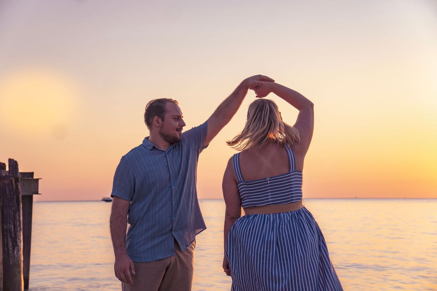 Couple dancing together at sunset by the ocean with a romantic orange sky in the background.