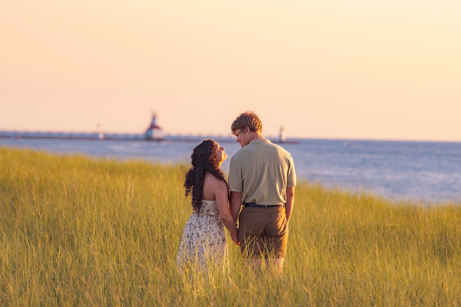 Romantic couple shares a tender moment in golden grass at sunset overlooking the ocean.