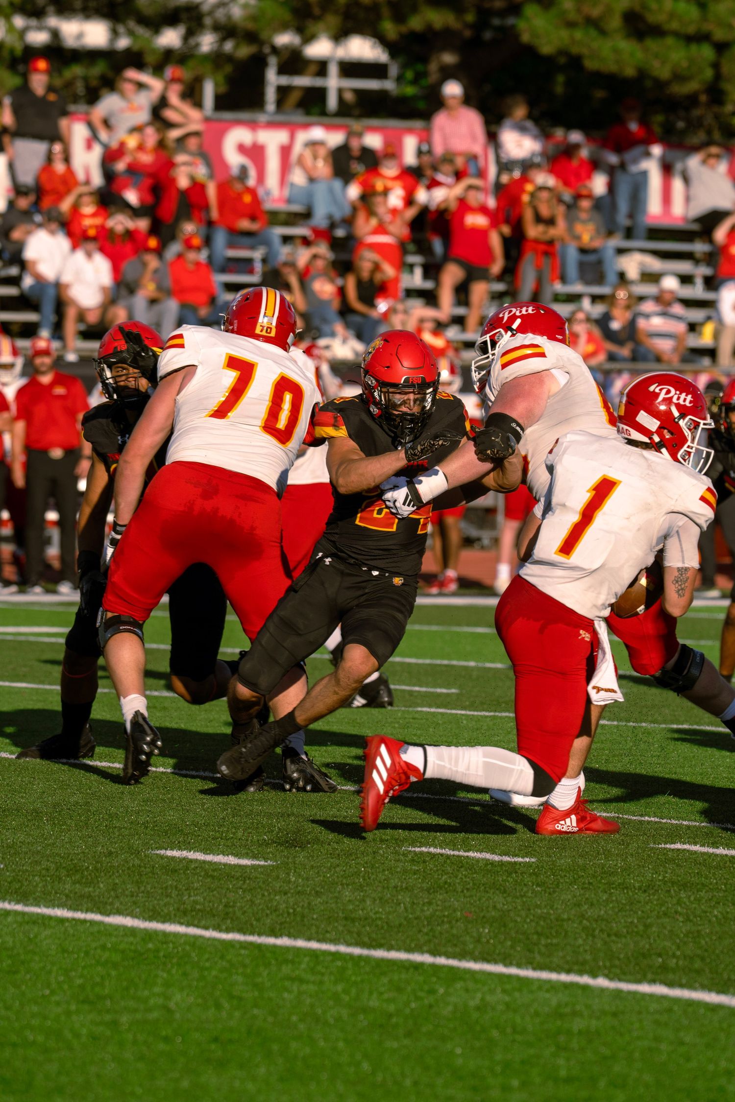 Football players engage in an intense line of scrimmage battle during a game between red and black uniformed teams.