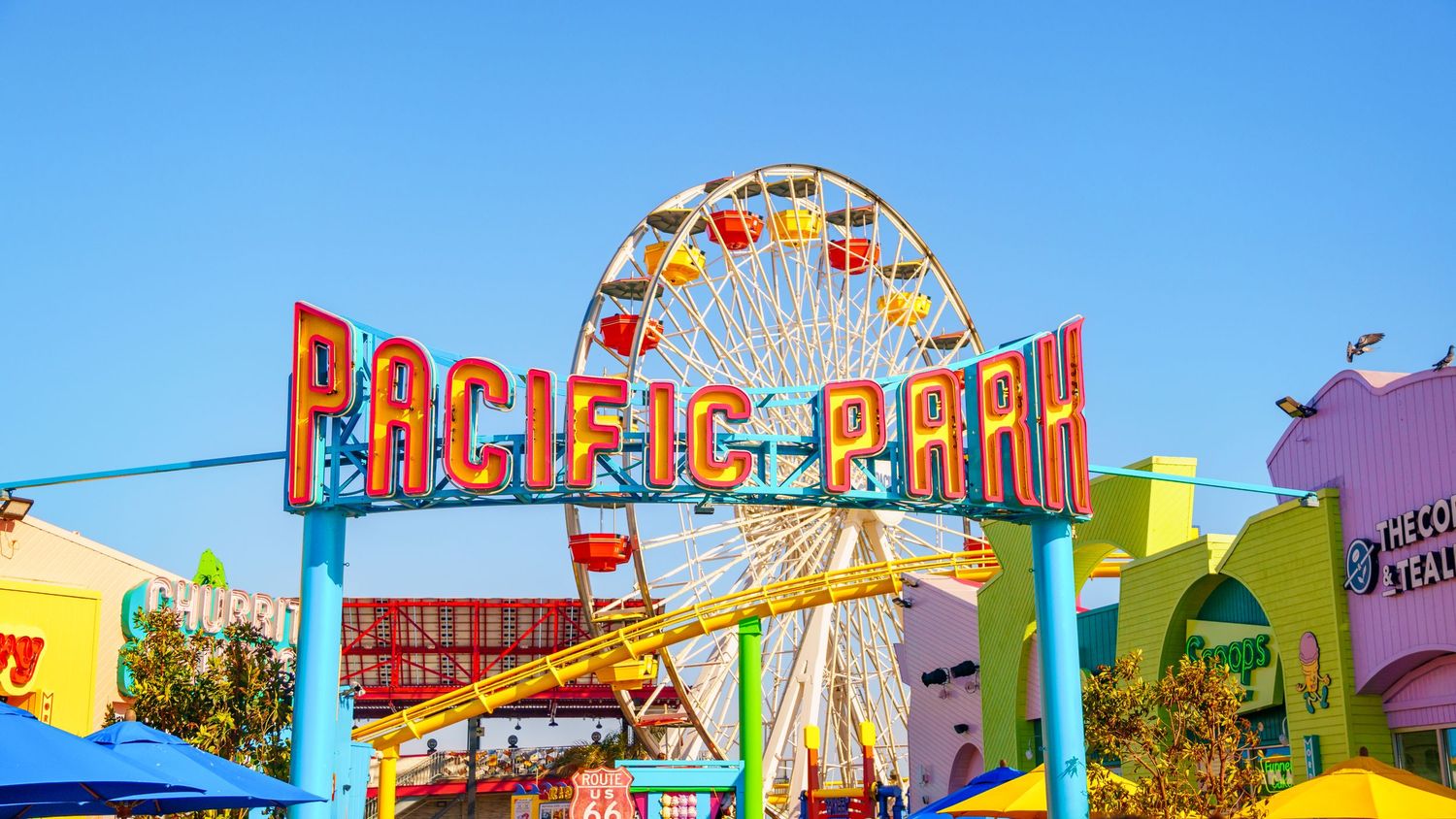 Iconic Pacific Park sign and Ferris wheel at Santa Monica Pier against vibrant blue sky.