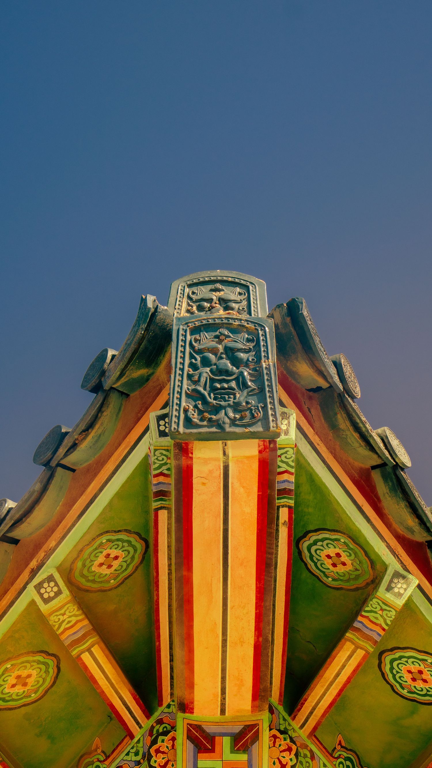 Ornate green and orange decorative roof detail of traditional Korean temple architecture against blue sky.