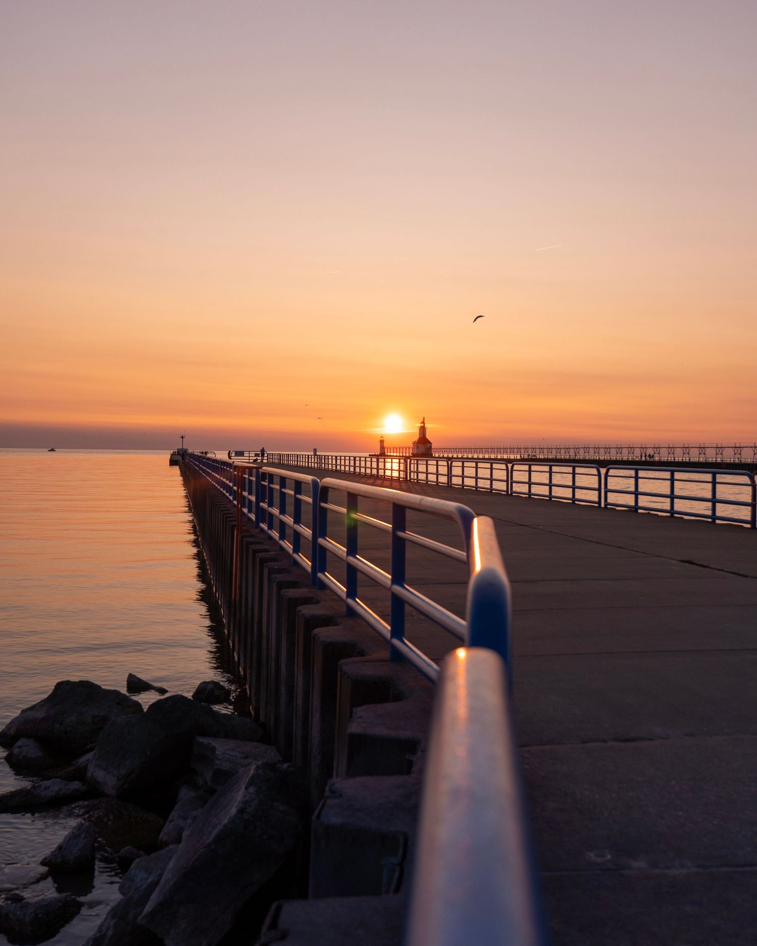 Long pier stretches toward setting sun with railing leading to horizon.