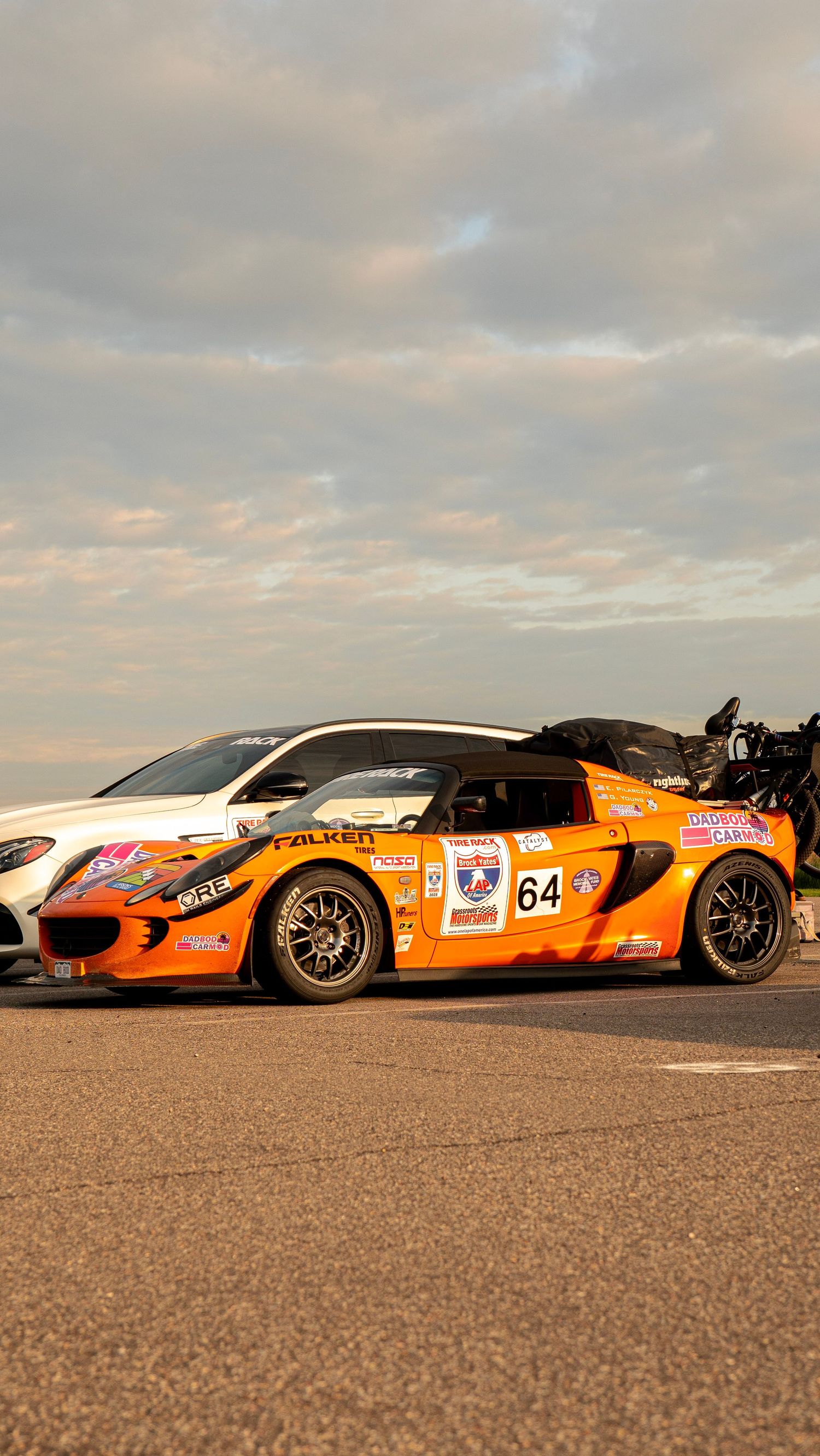 Orange and black race car with number 64 and sponsorship decals in sunset lighting.