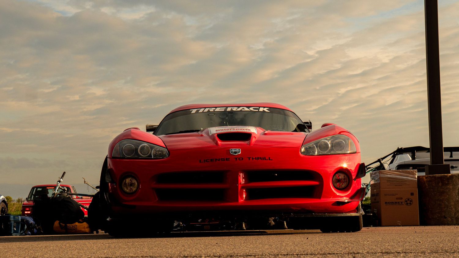 Head-on view of red Dodge Viper with racing modifications under cloudy sky.