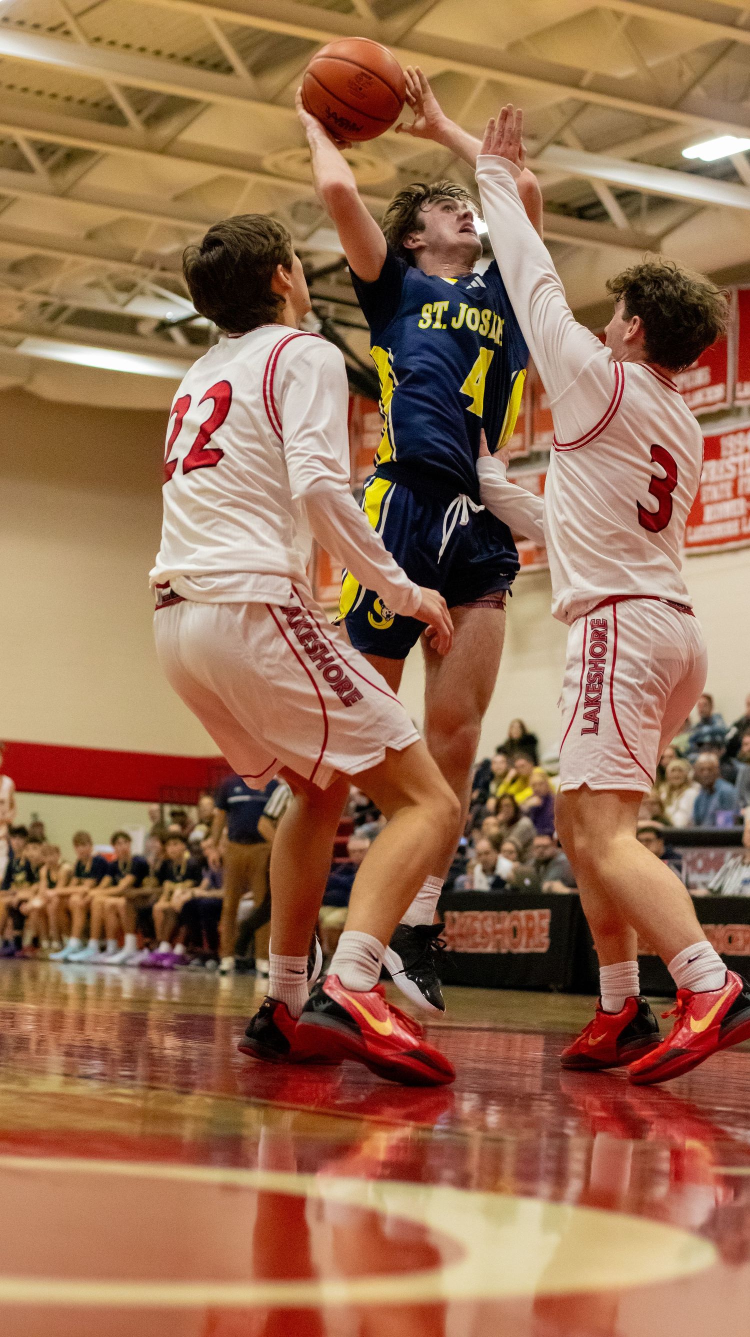 Basketball player in navy jersey leaps between two defenders in white uniforms during intense game action.