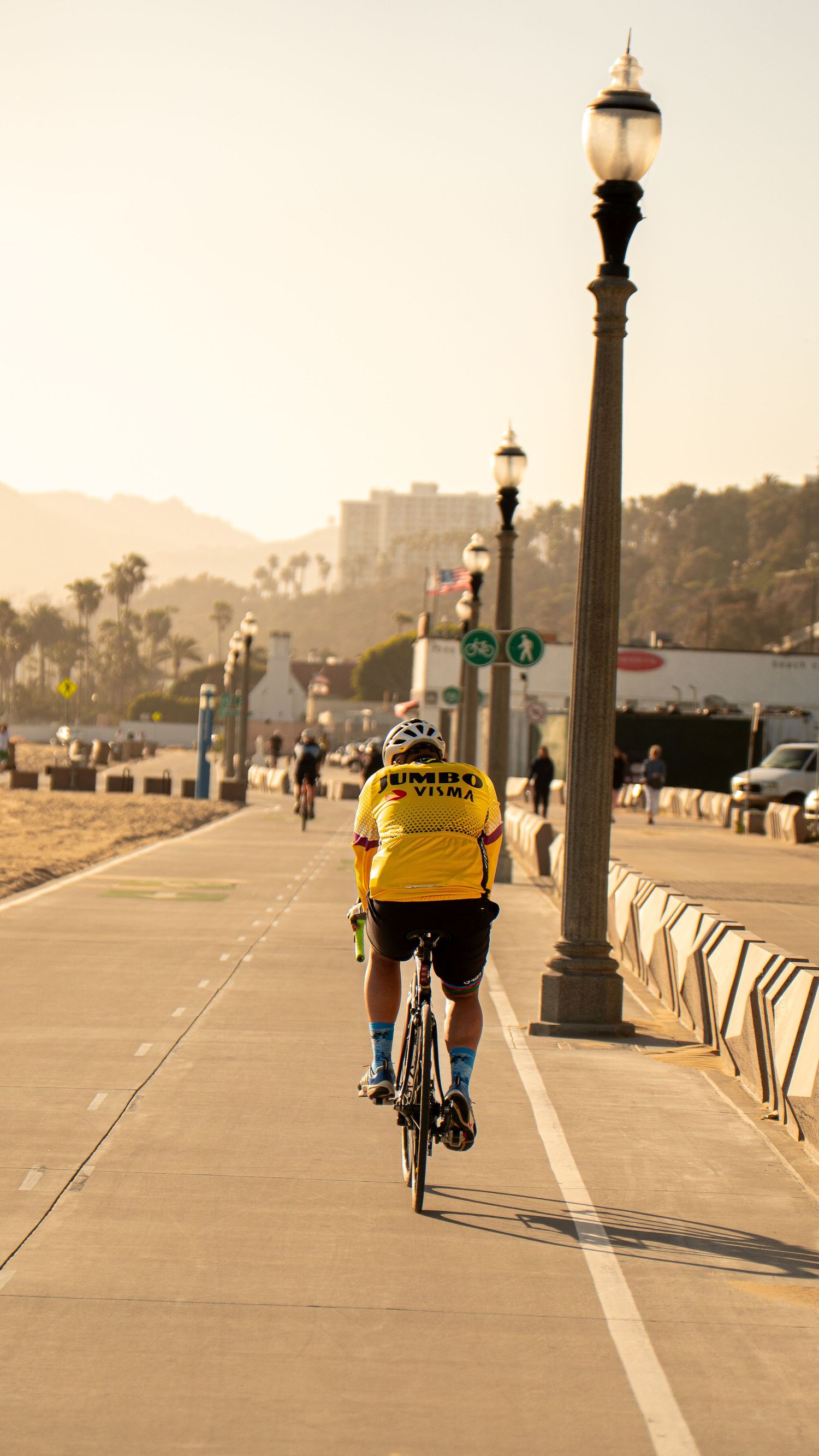 Cyclists riding along empty beachfront path during golden hour.
