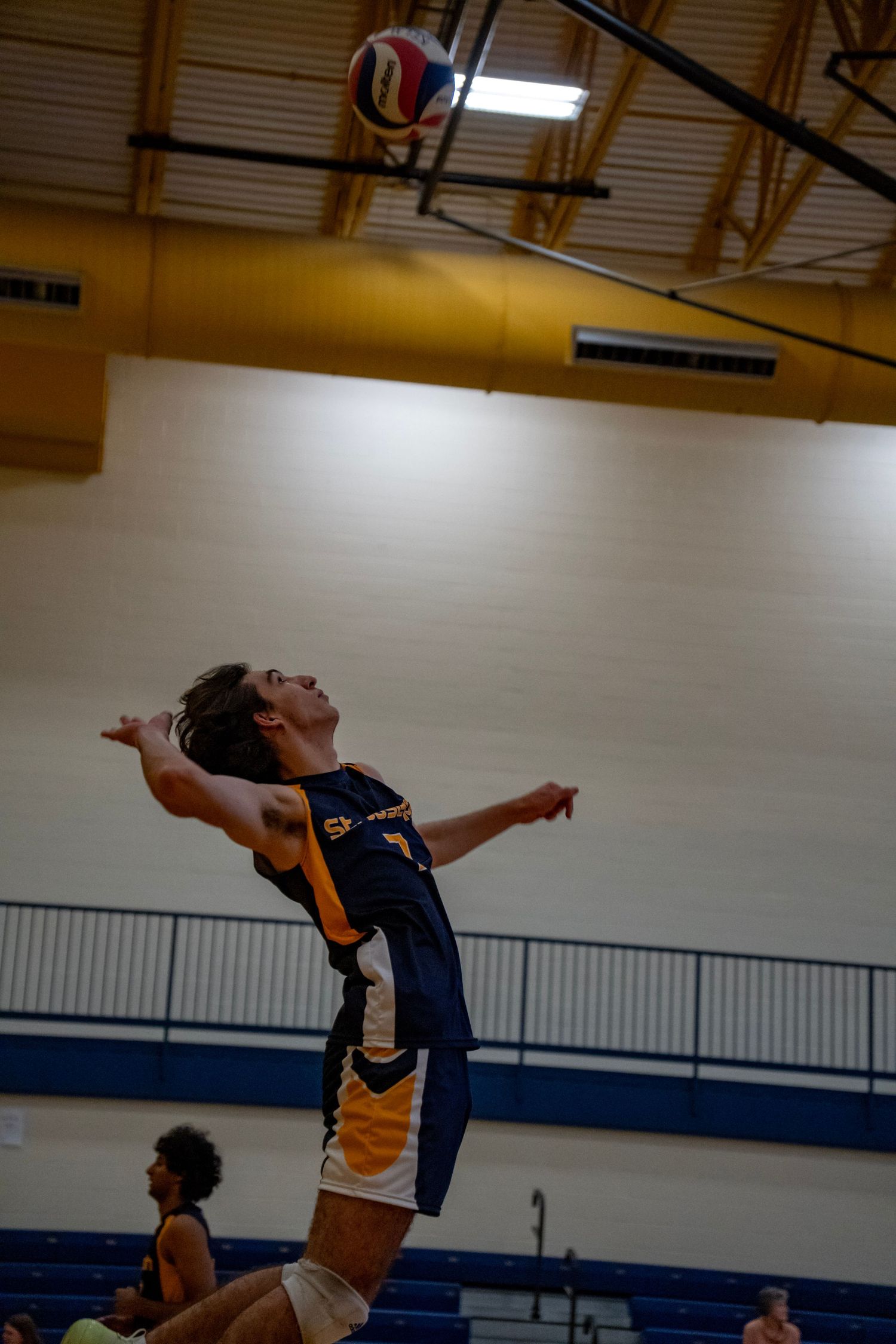 Volleyball player arches backward to serve the ball during an indoor match.