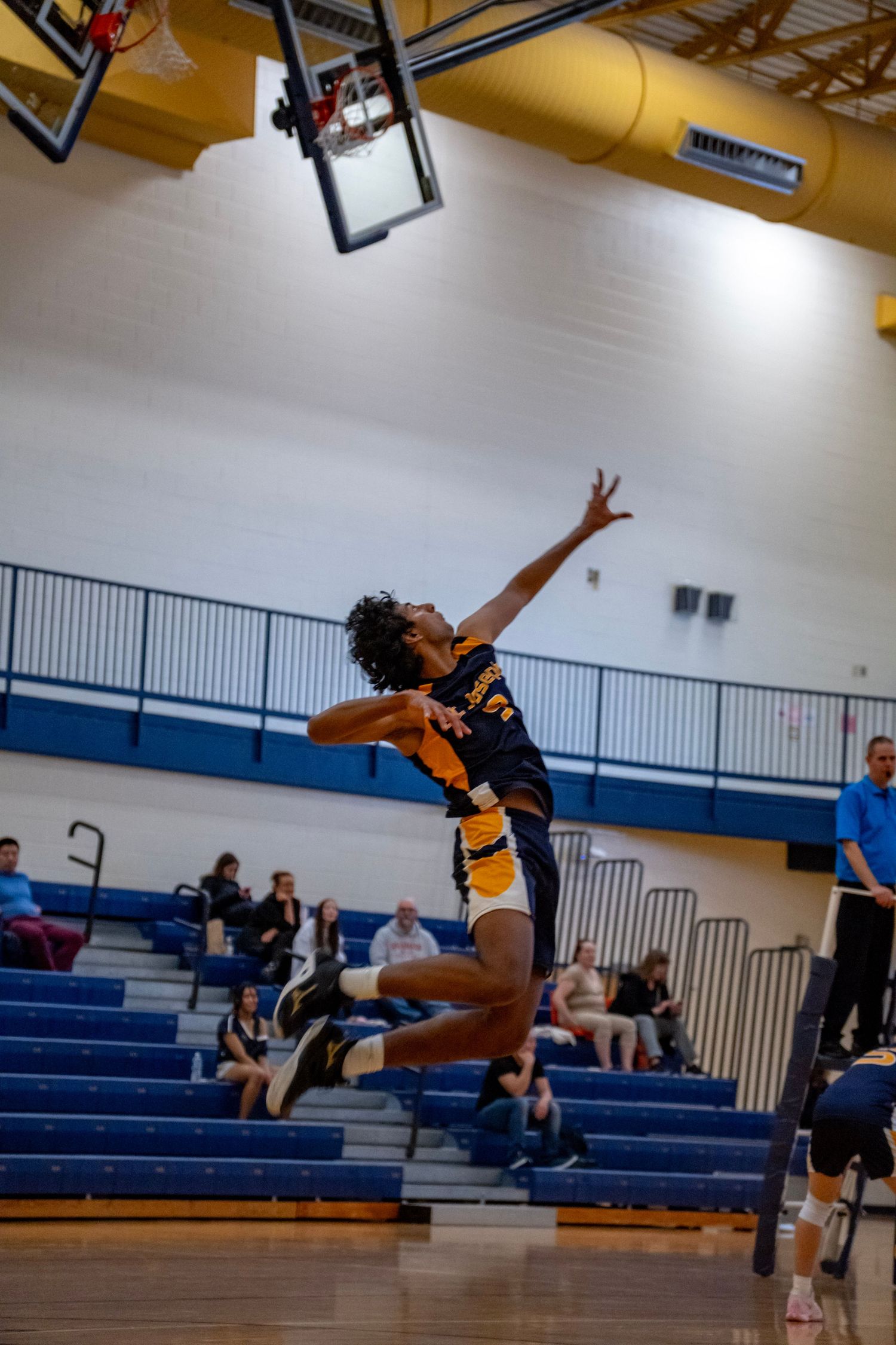 Athletic player jumps with extended arm to hit volleyball in school gymnasium.