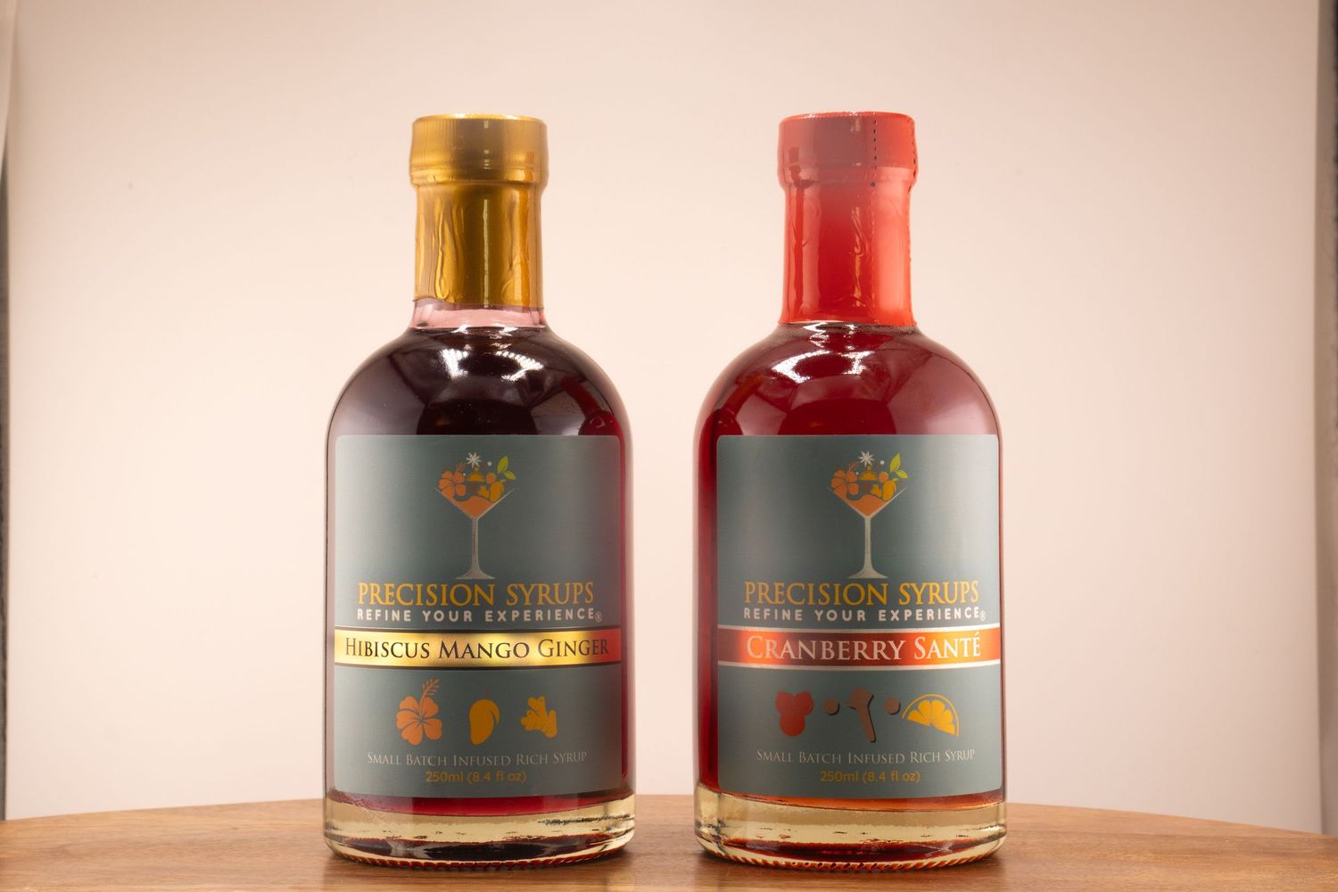 Two artisanal spirits bottles with gold and red caps displayed side by side on wood surface.