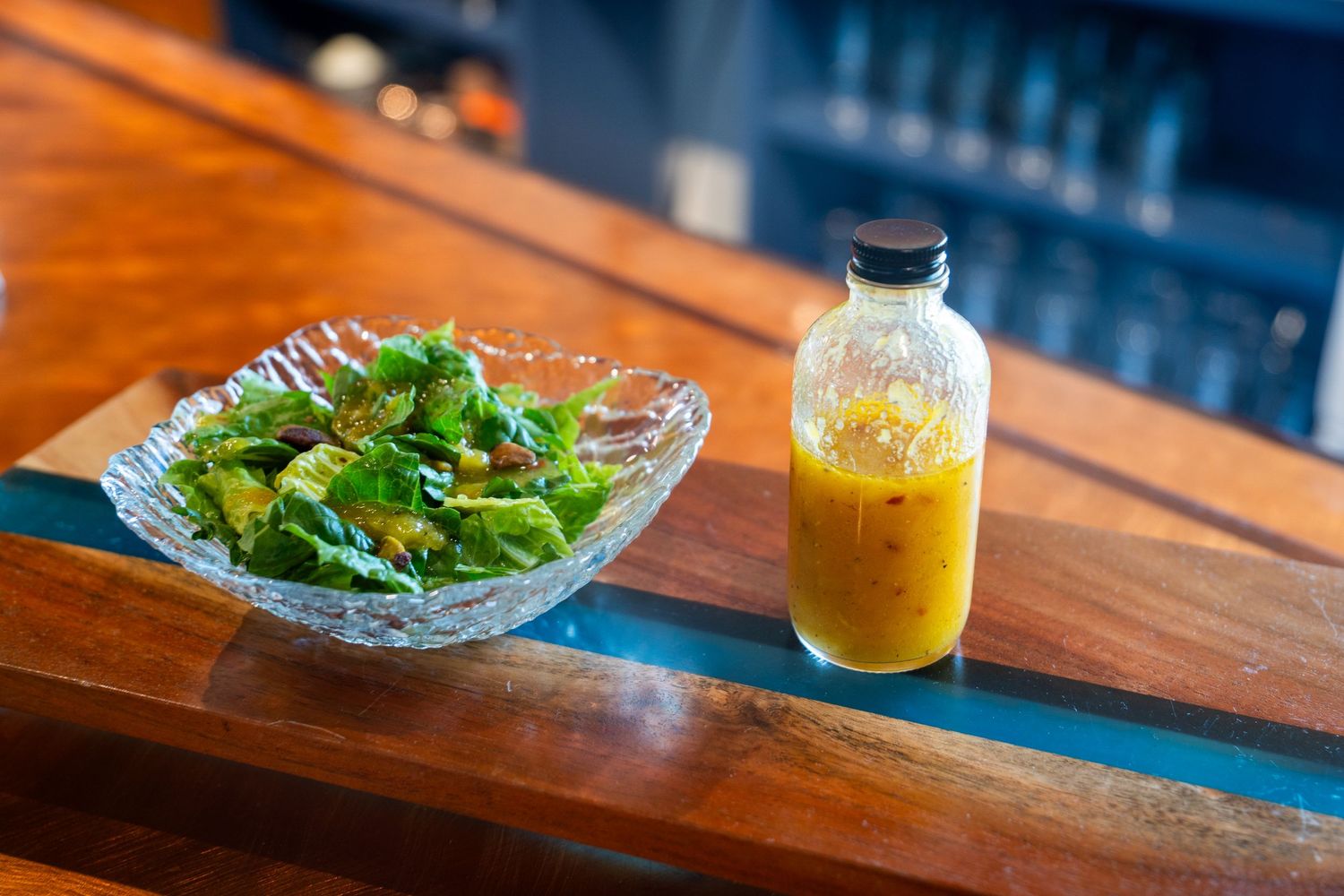 Fresh green salad in crystal bowl with homemade dressing in glass bottle on wooden bar counter.