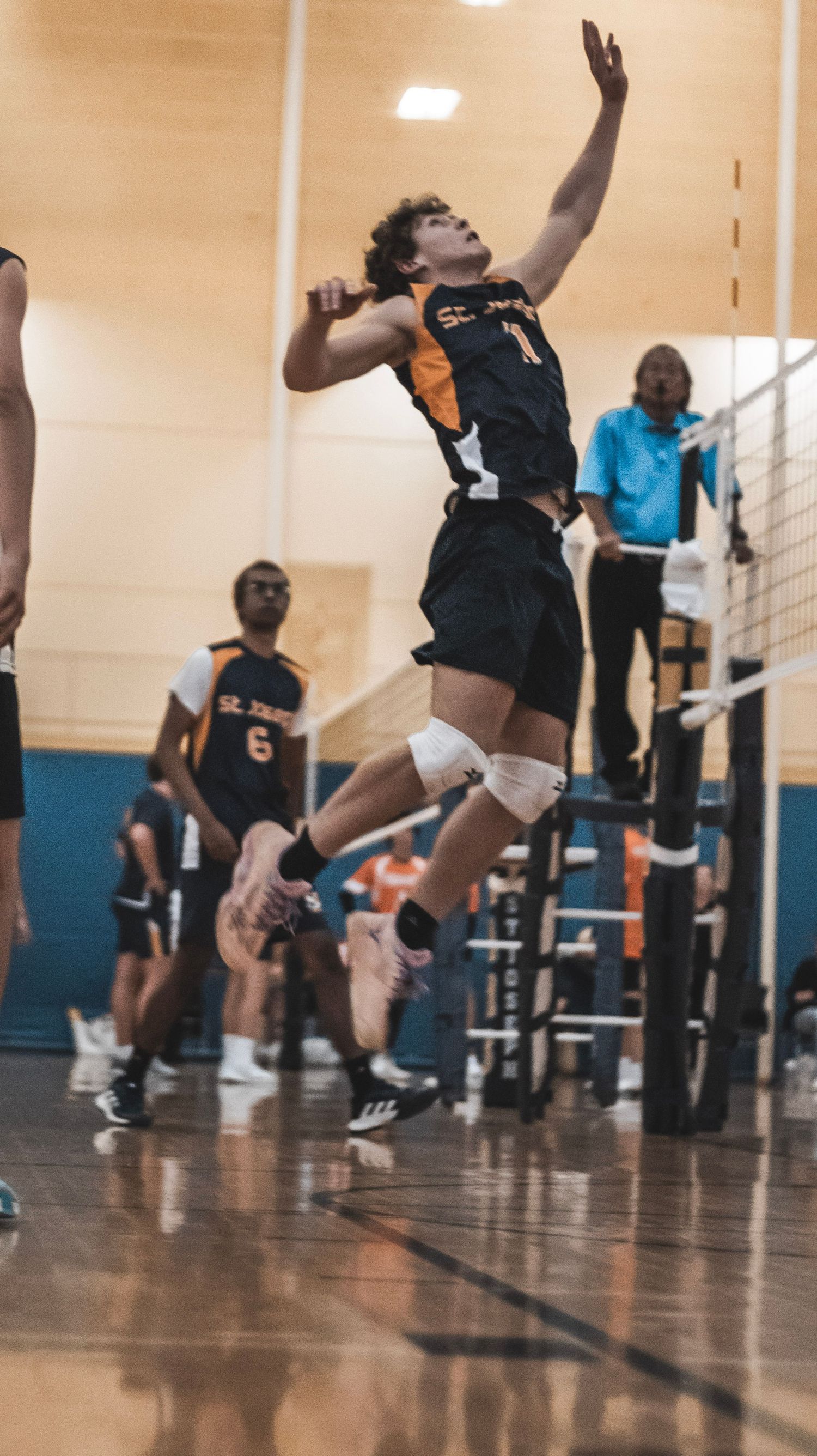 A player in a black and orange uniform leaps to spike the volleyball during an indoor match.