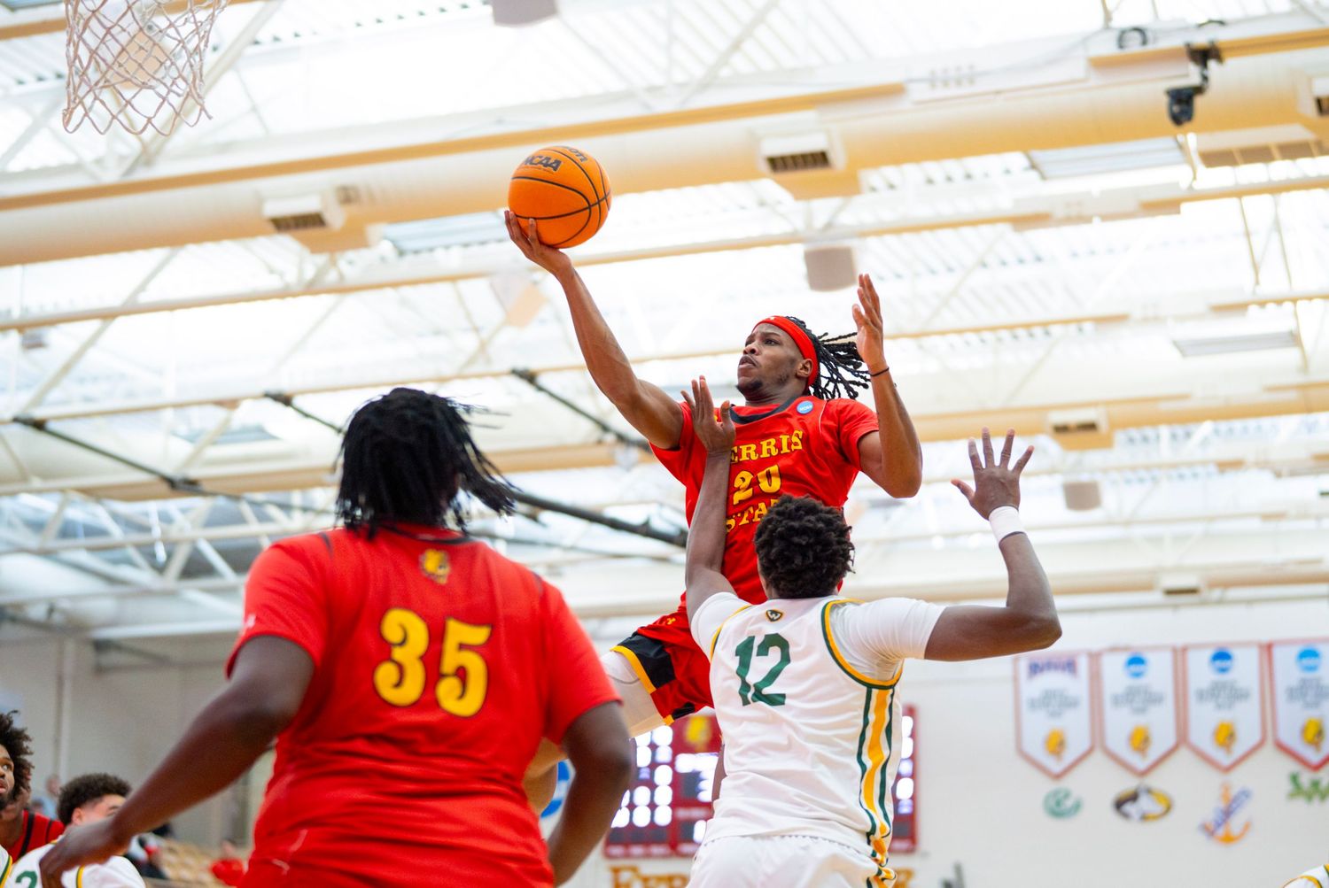 Basketball player in red jersey leaps high for a layup during intense indoor game action.
