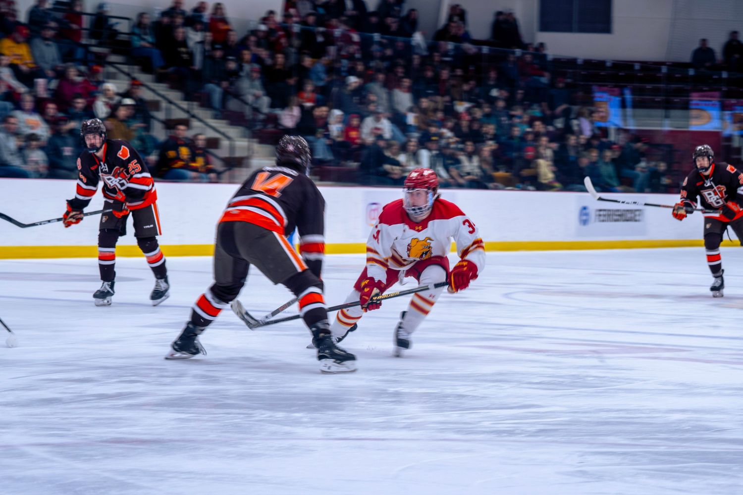 Ice hockey players in red and black jerseys compete during a fast-paced game on a rink.
