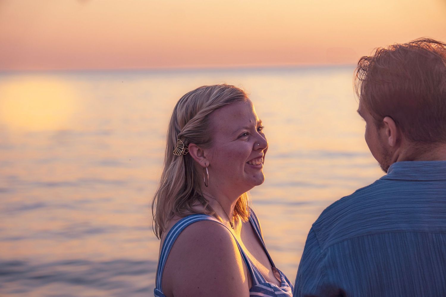 Two people embrace while standing outdoors during a vibrant sunset with pink and orange skies.