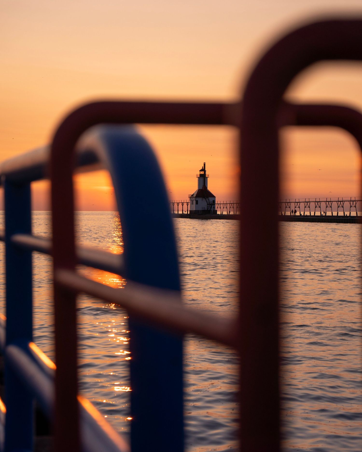 Lighthouse silhouette framed by railing during golden sunset over Lake Michigan.