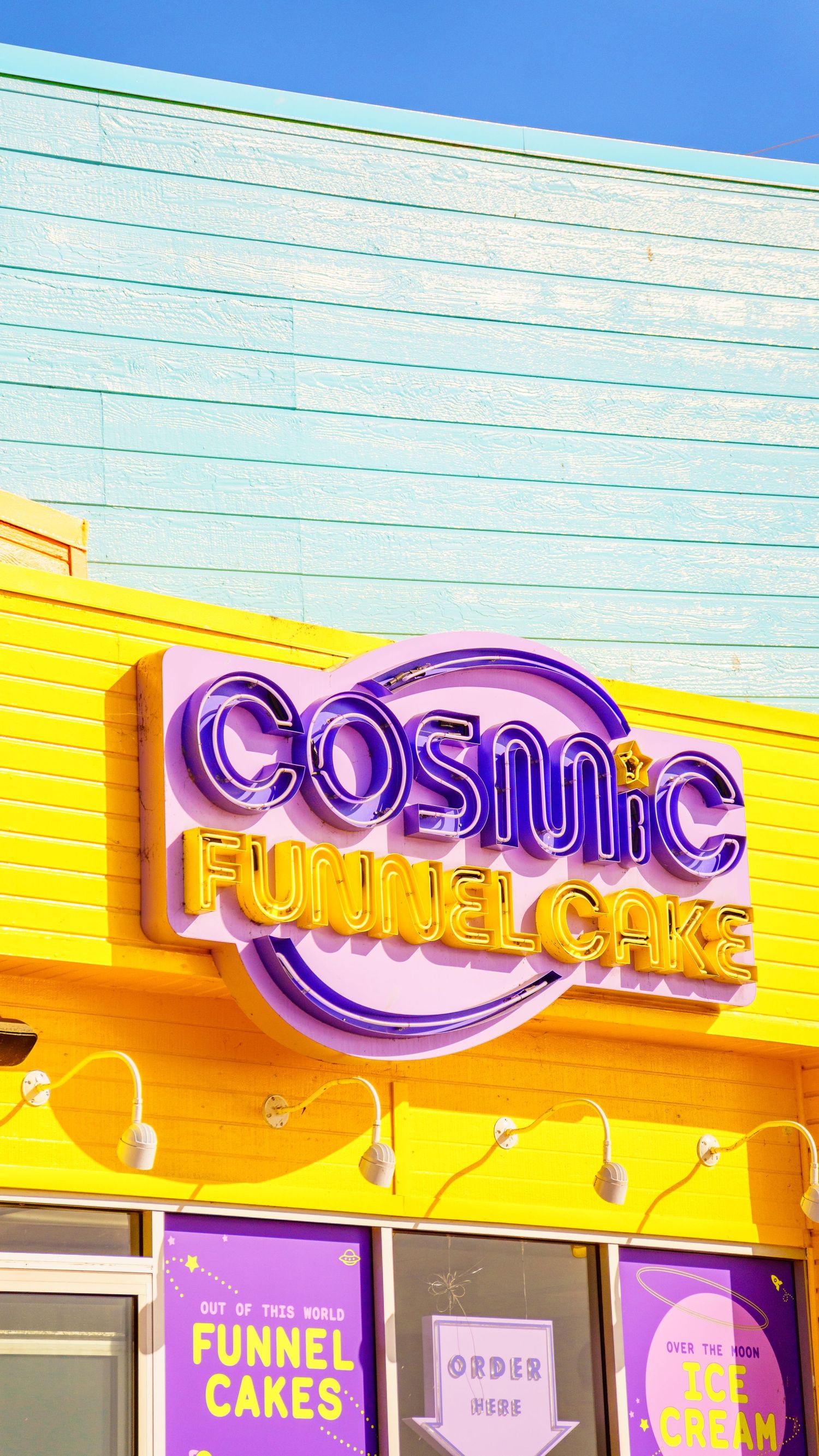 Purple and yellow Cosmic Funnel Cake shop sign mounted on colorful building exterior.