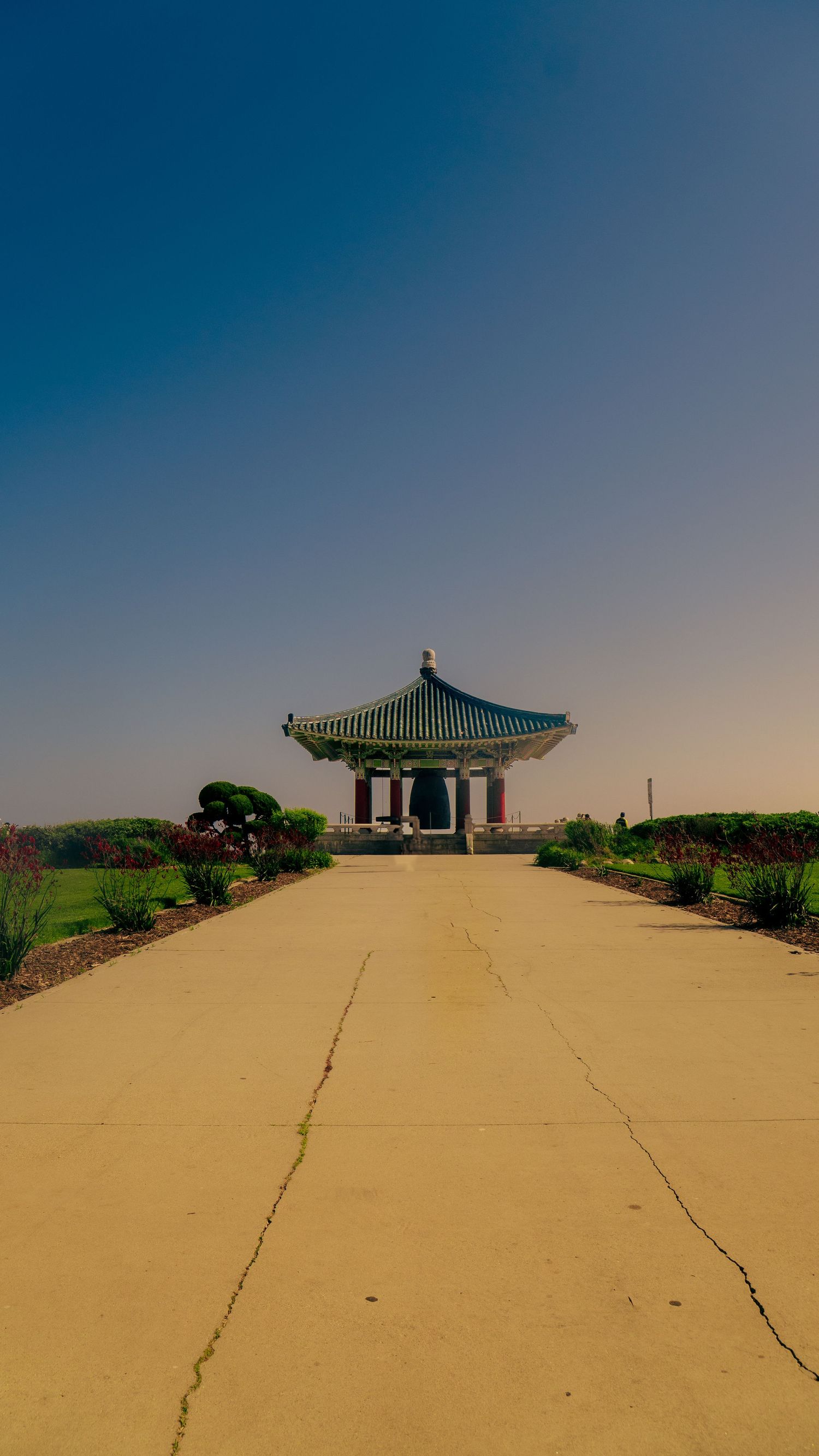 Traditional Korean pavilion with green tiled roof sits atop a yellow concrete platform in bright daylight.