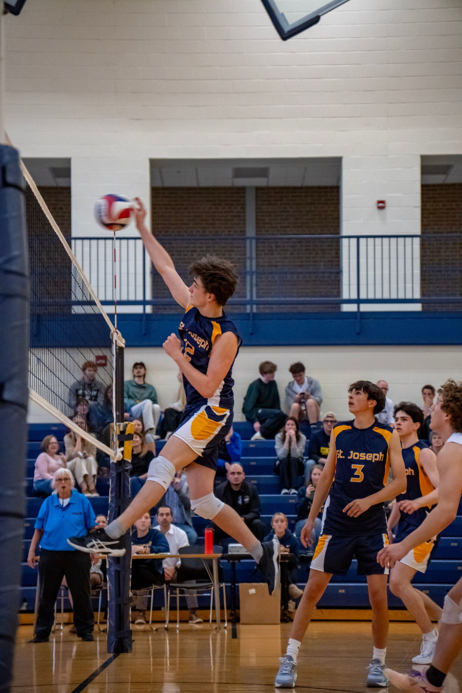 A volleyball player leaps high to spike the ball during a competitive indoor match.