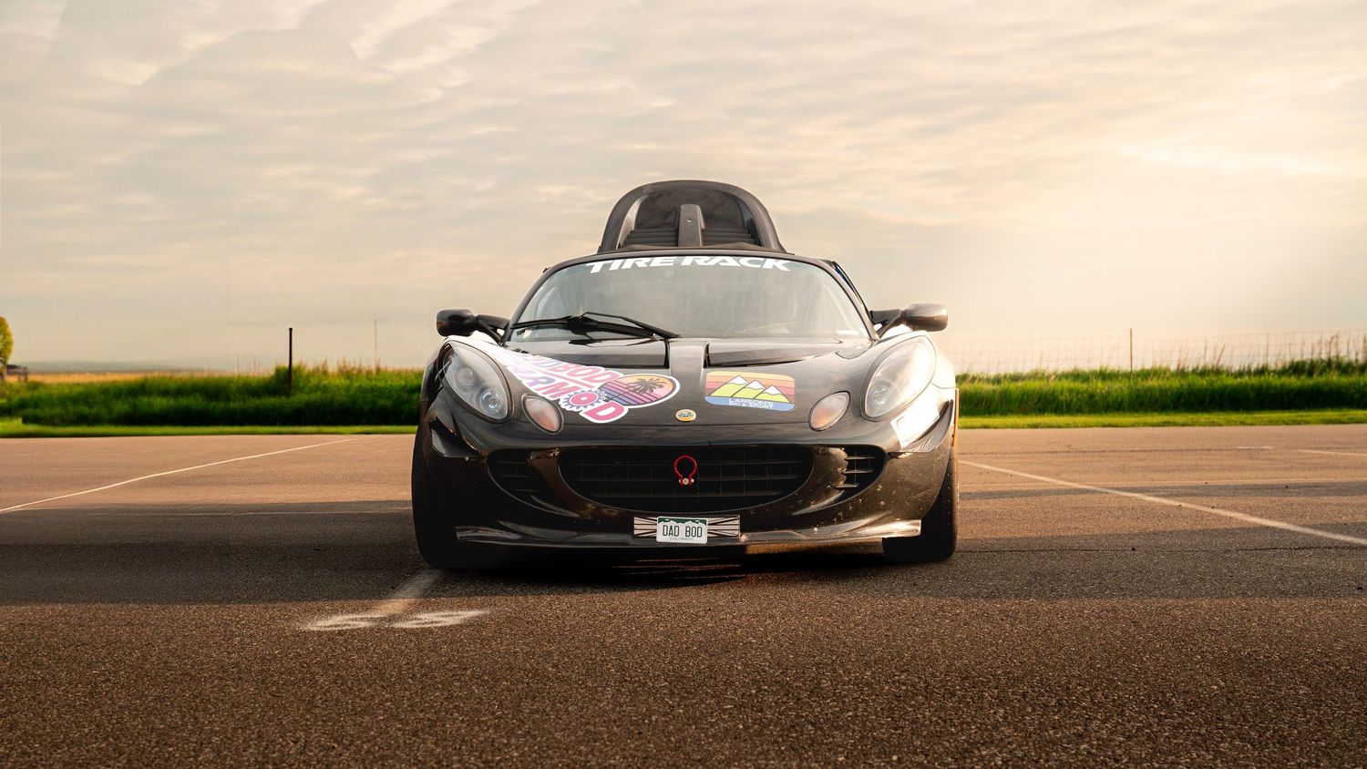 Head-on view of black Lotus sports car on racing track at dusk.