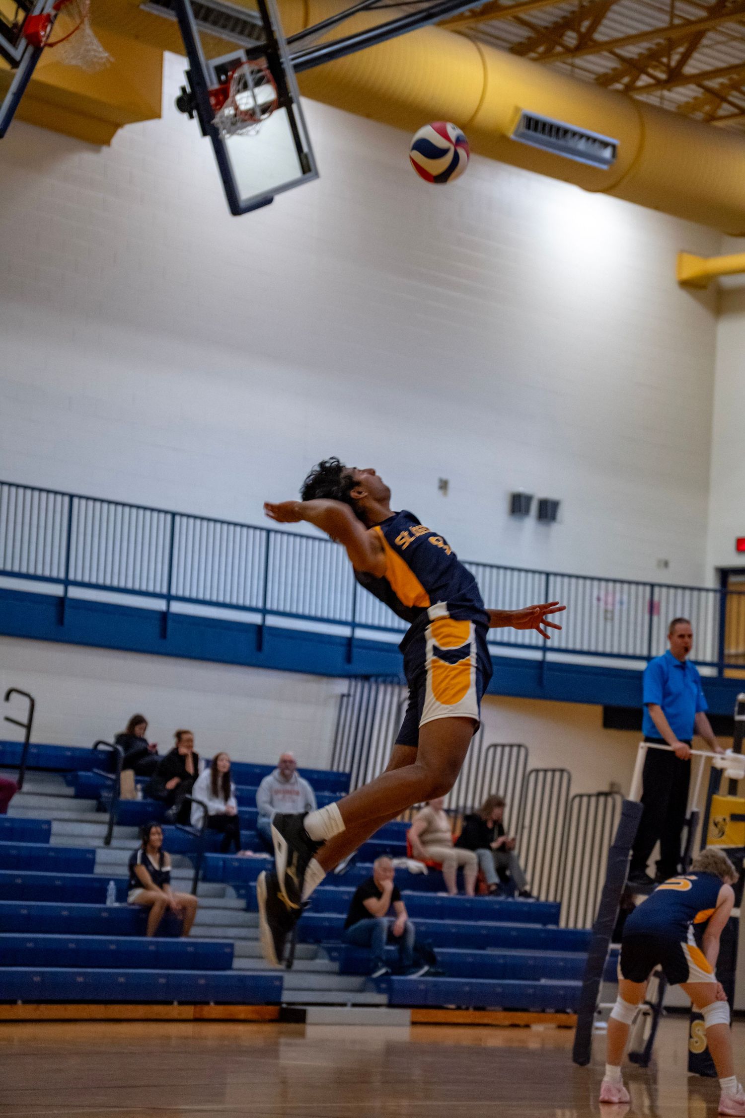 Player executes powerful jump serve during volleyball match in gymnasium.