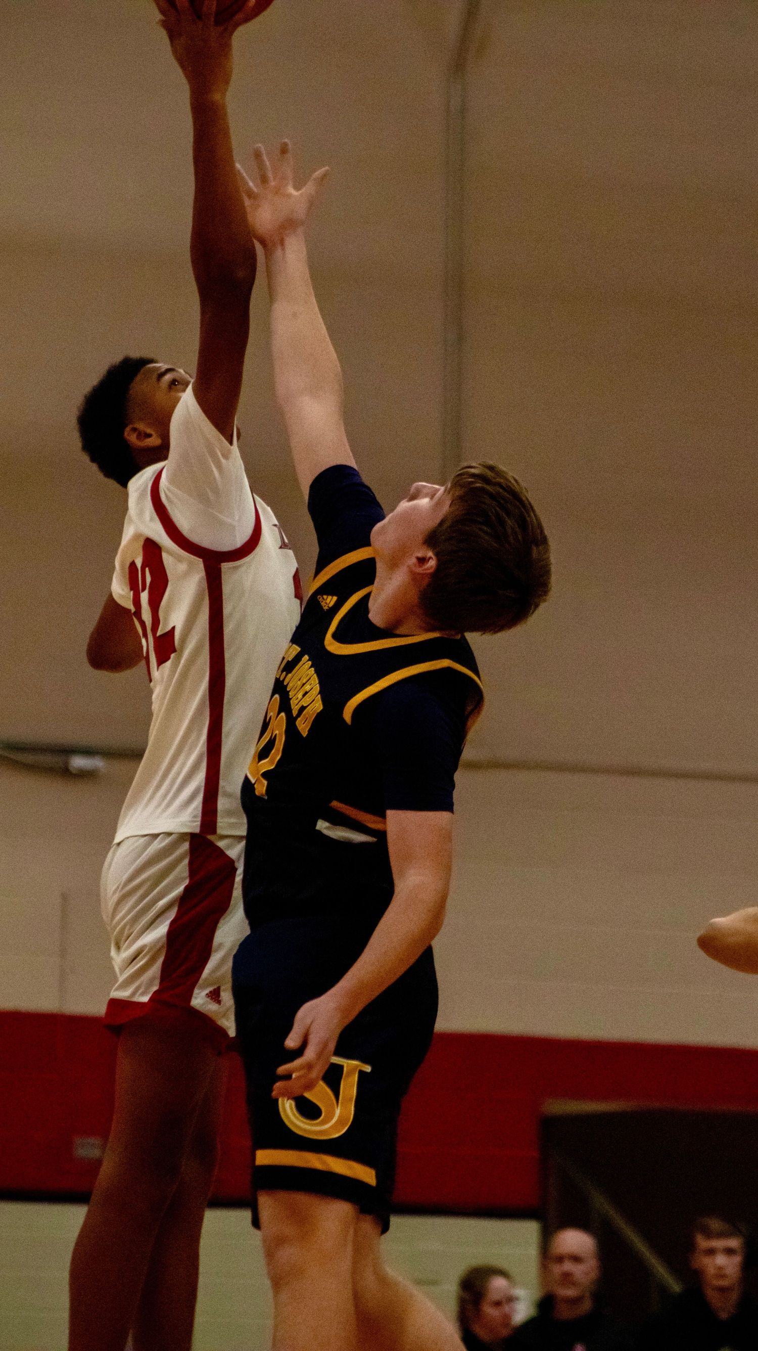 Two basketball players jump high to compete for a rebound during indoor game.