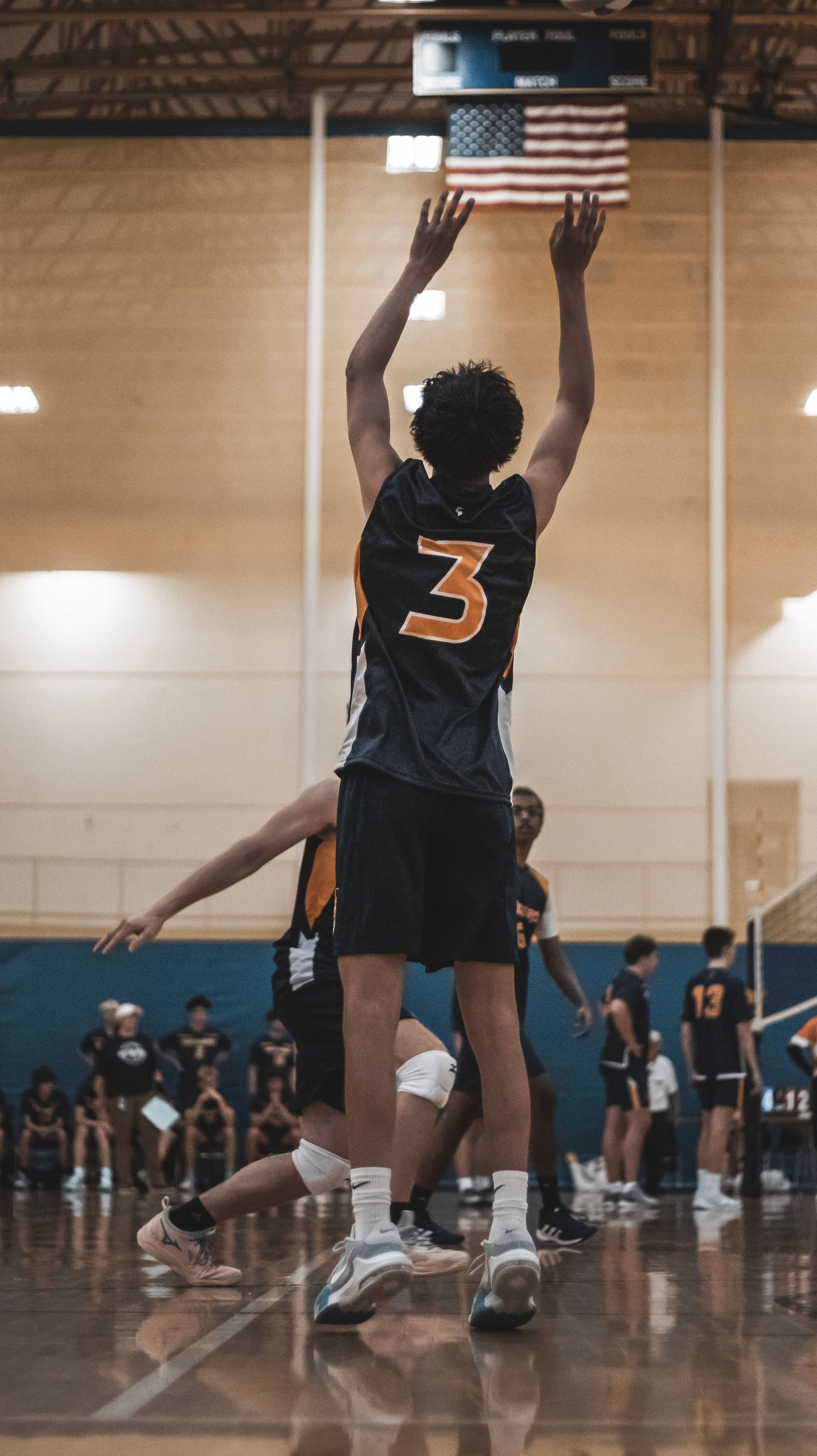 A player wearing jersey number 3 jumps to serve the volleyball during an indoor match.